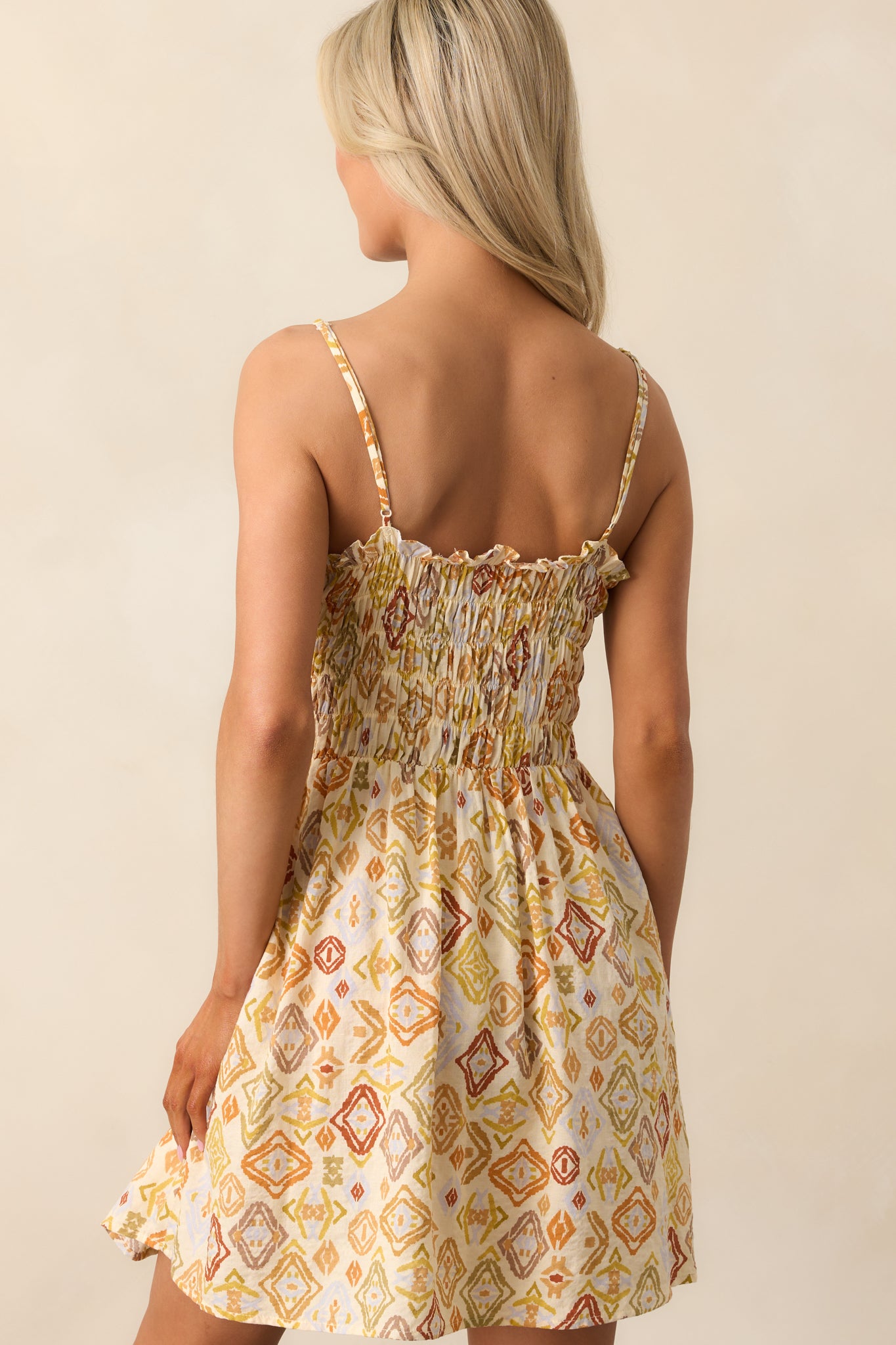 The beige mini dress viewed from behind, showcasing the adjustable straps, smocked detailing, and flowy silhouette.