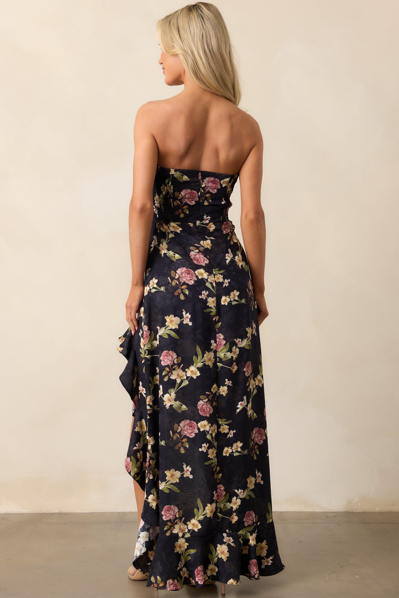 A black strapless dress with smocked back panels, a hidden zipper closure, and a high-low hem, highlighting the design from behind.