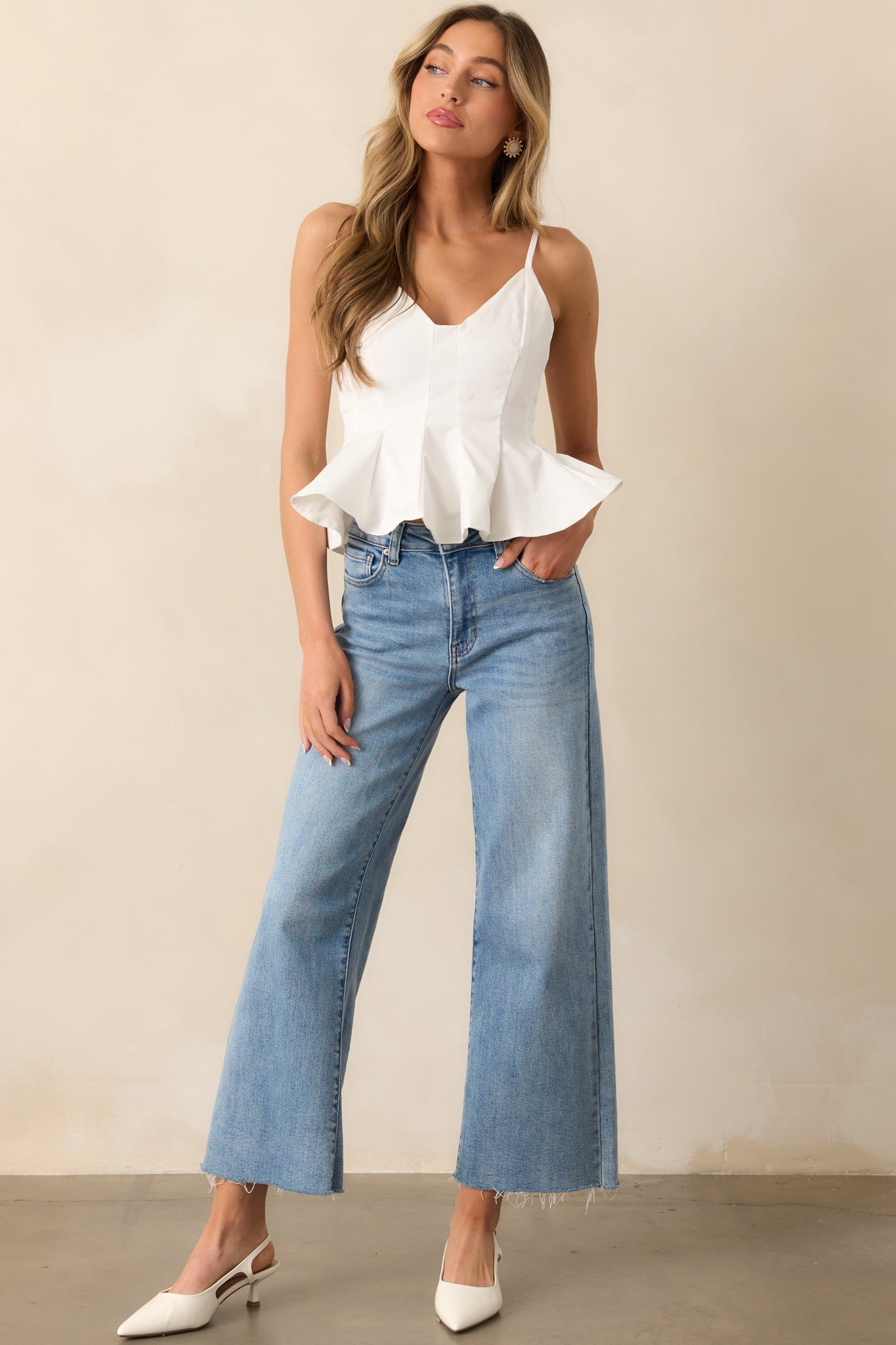 The white top showcasing the v-neckline, adjustable spaghetti straps, and the structured peplum silhouette, paired with a panel design and cropped length that accentuate a chic, feminine silhouette.