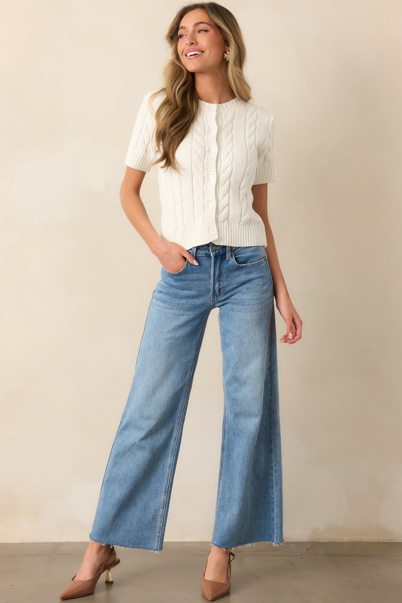 A delicate ivory cardigan featuring a functional button front, textured cable knit fabric, and a flattering fitted silhouette.