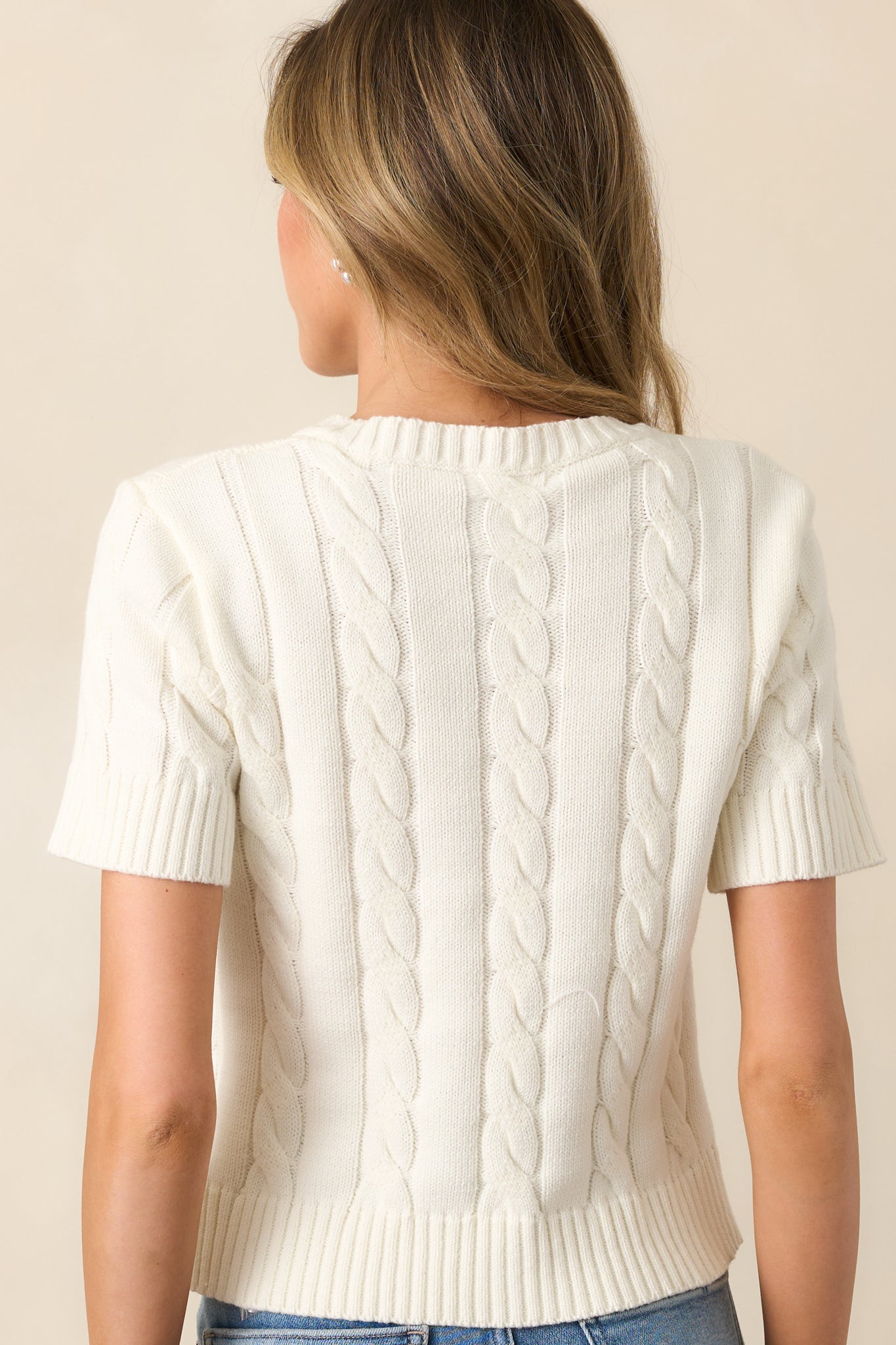 The ivory cardigan’s fitted cable knit design and ribbed hems continue on the back for a seamless look.