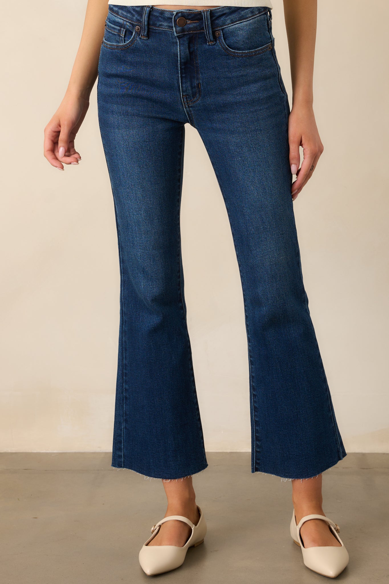 Close-up of the waistband on the dark wash jeans, highlighting the button-zipper closure, belt loops, and high-waisted fit.