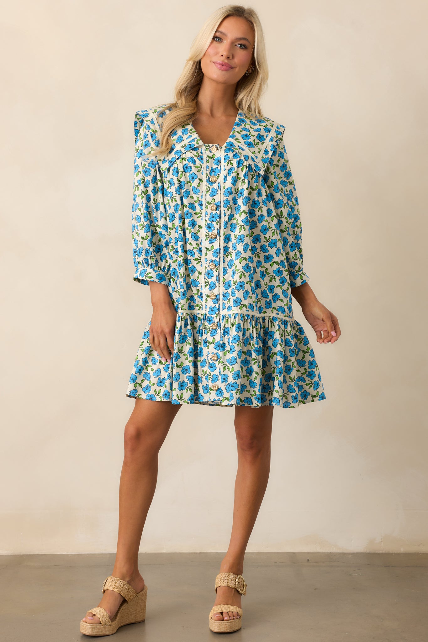 A blue mini dress with a peter pan collared neckline, button front design, floral print, and 3/4 sleeves.