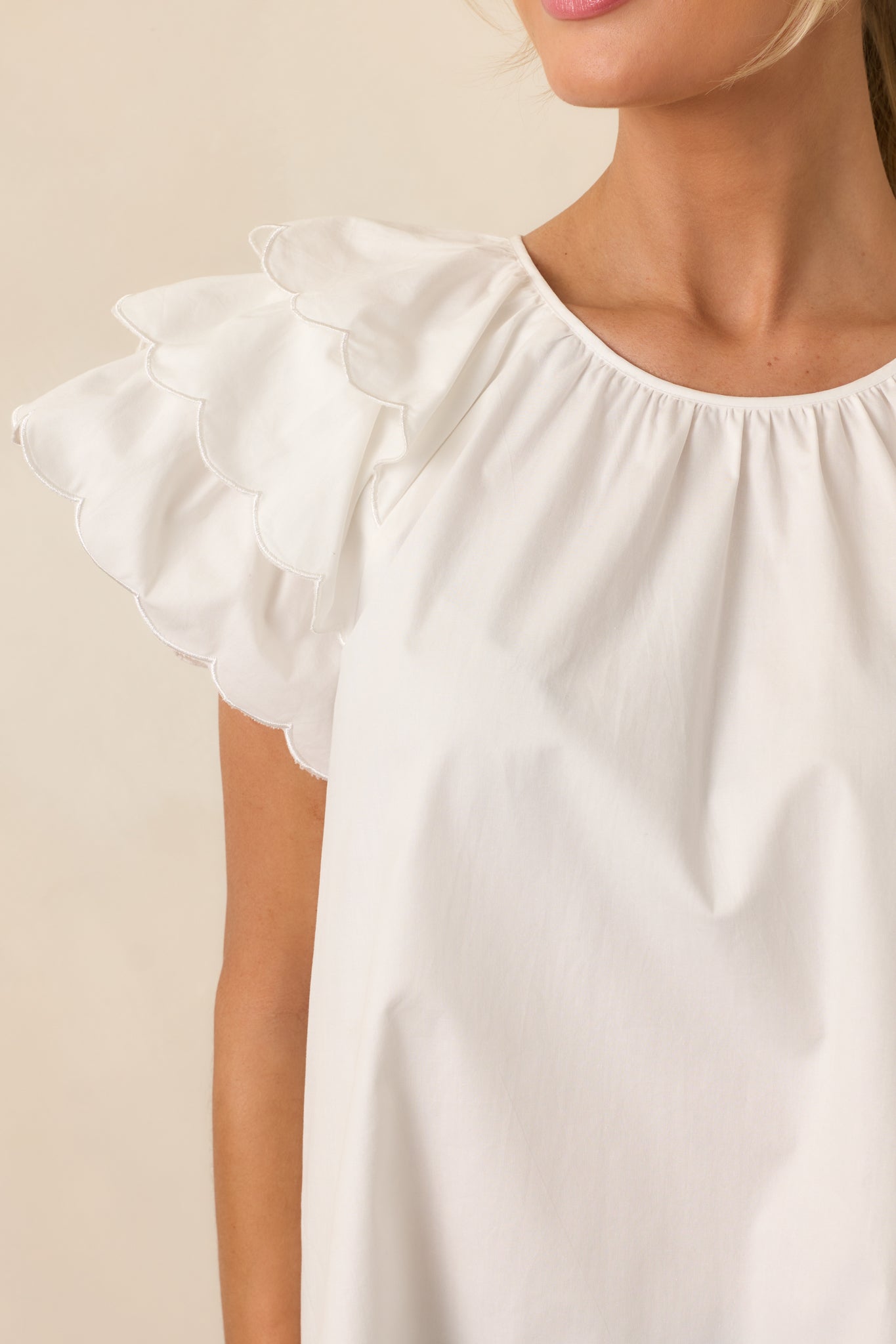 A close-up showing the soft fabric, layered flutter sleeves, and scalloped hems of the white top, highlighting its intricate details.