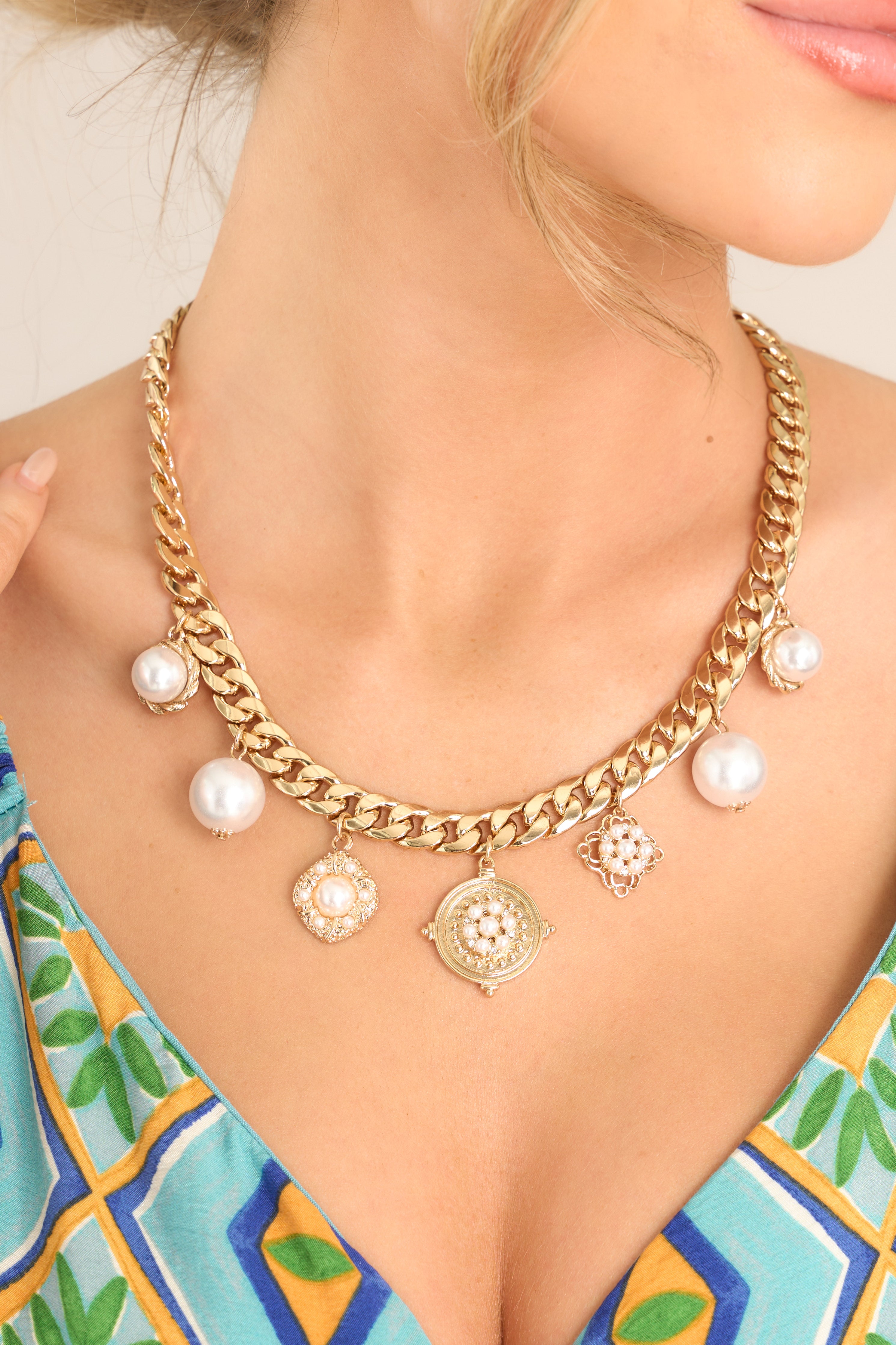 This necklace features gold hardware, a chunky curb chain, large faux pearl & gold pendants, and a lobster claw closure.