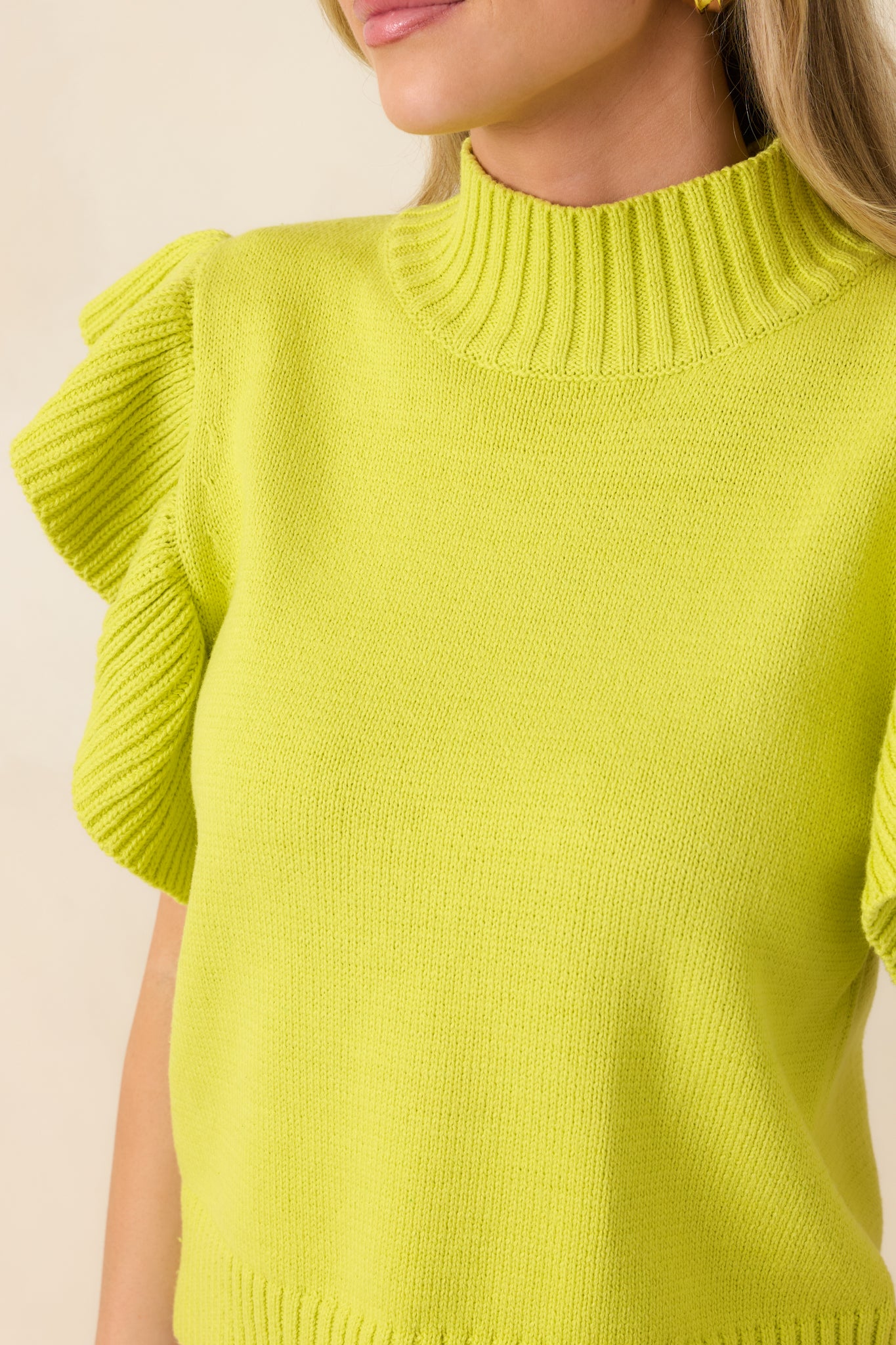 Close-up of the yellow-green knit fabric revealing ribbed texture at the mock neckline, flutter sleeves, and hem.