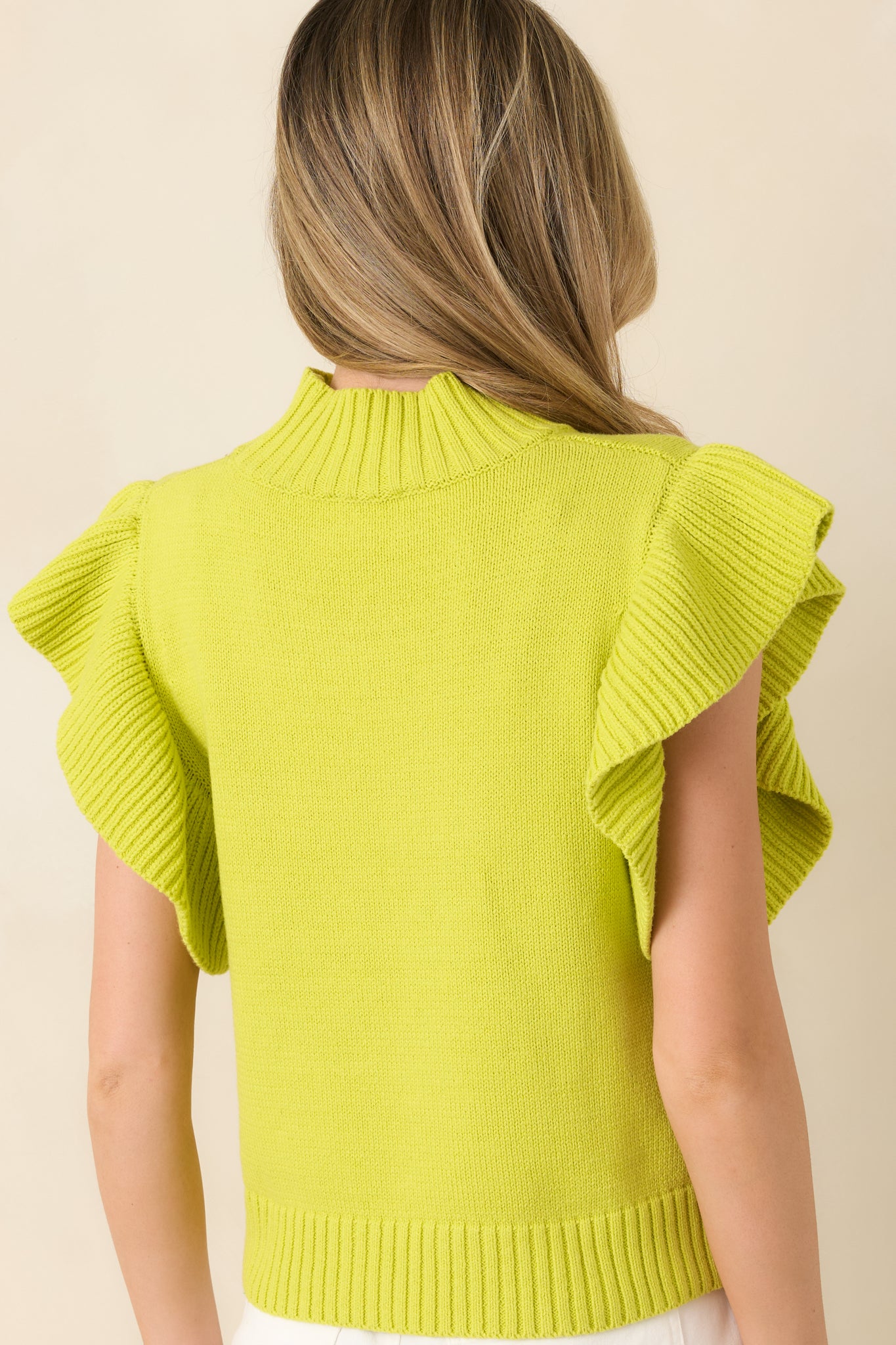 Rear view of the yellow-green top displaying the ribbed mock neckline, flutter sleeves, and smooth knit finish.