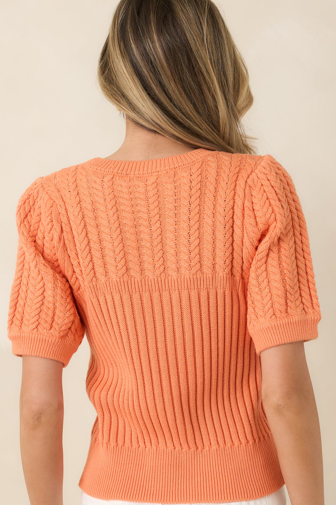 Rear view of the ribbed sweater featuring a fitted body, puffed short sleeves, and cable knit texture from behind.