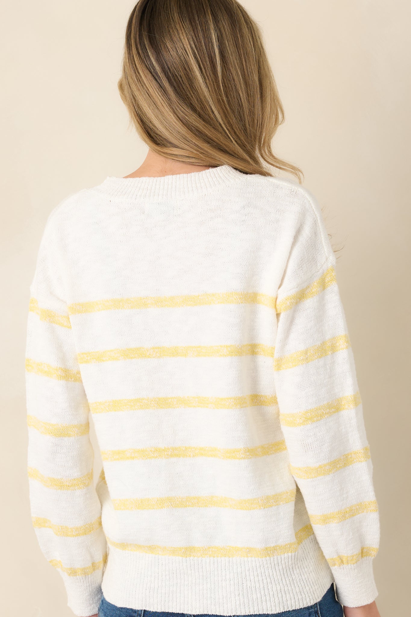 Rear view of the ivory sweater displaying yellow stripe accents and ribbed trim along the hem and cuffs.