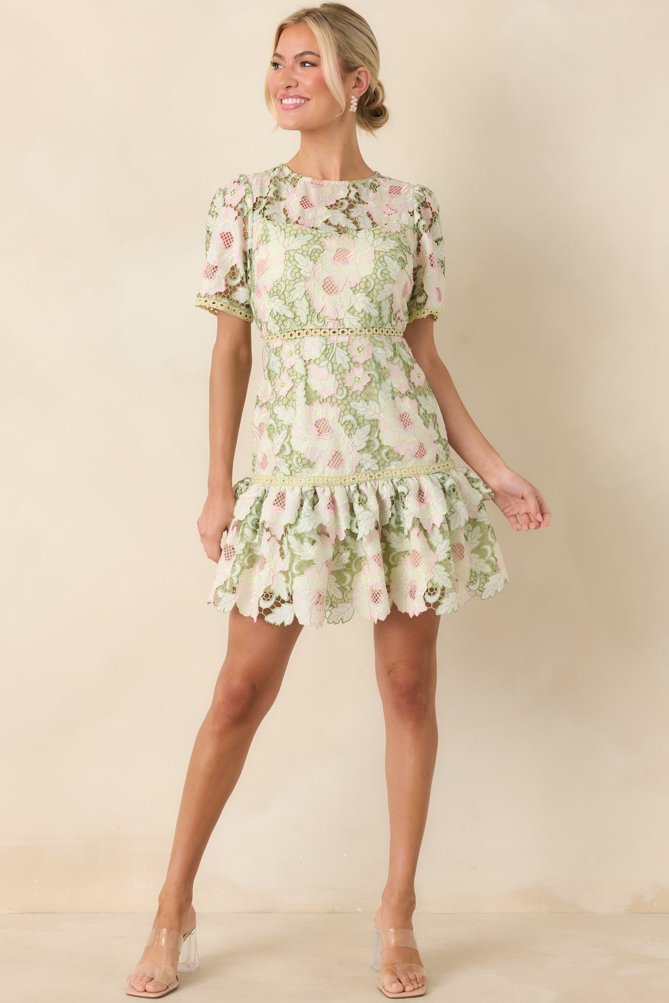 Romantic lace mini designed with intricate green blooms, a defined waist trim, and a softly flared ruffle hemline.