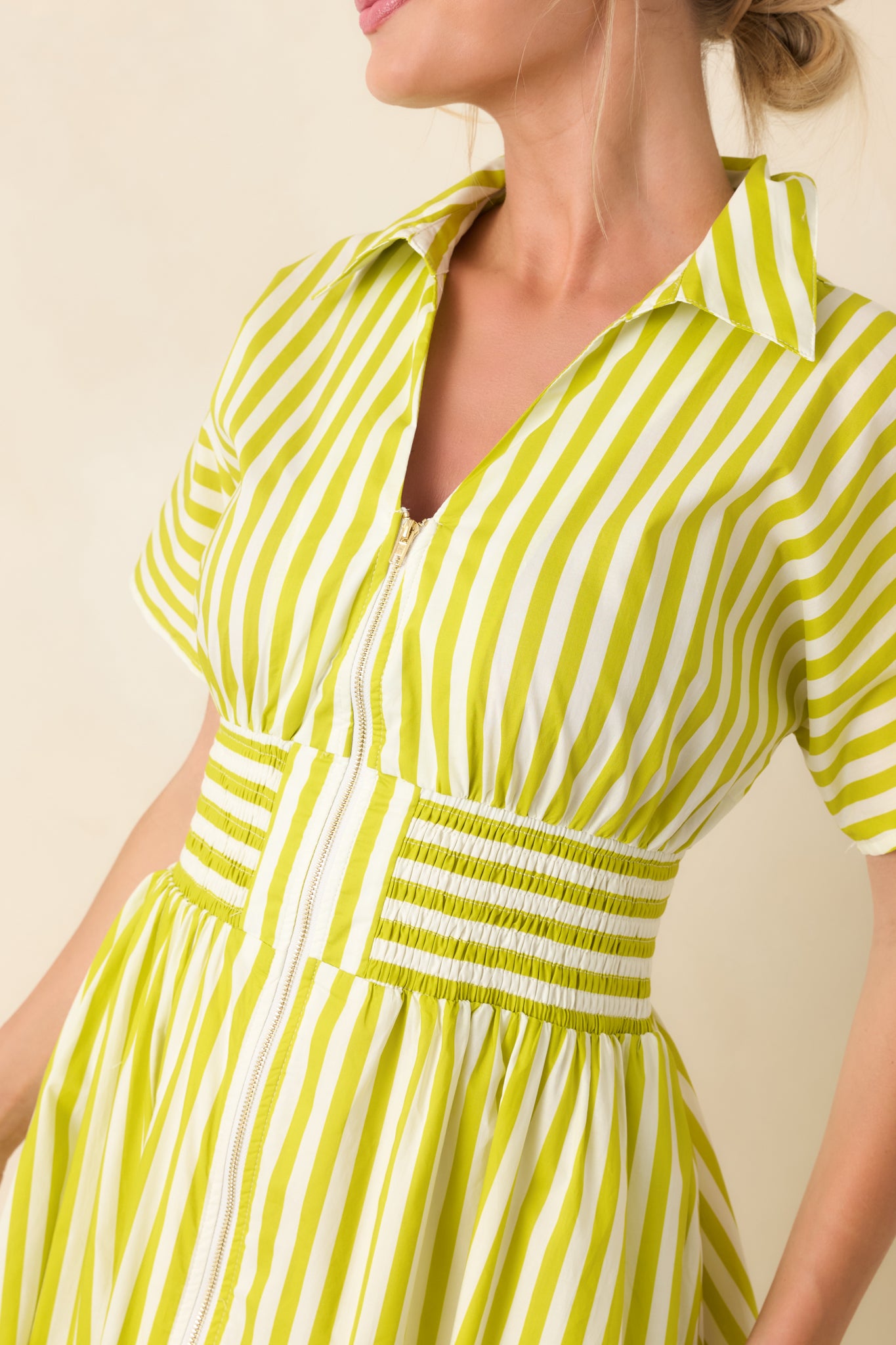 Close-up showing the green and white woven fabric, structured collared neckline, zip-front closure, and smocked waistband shaping.