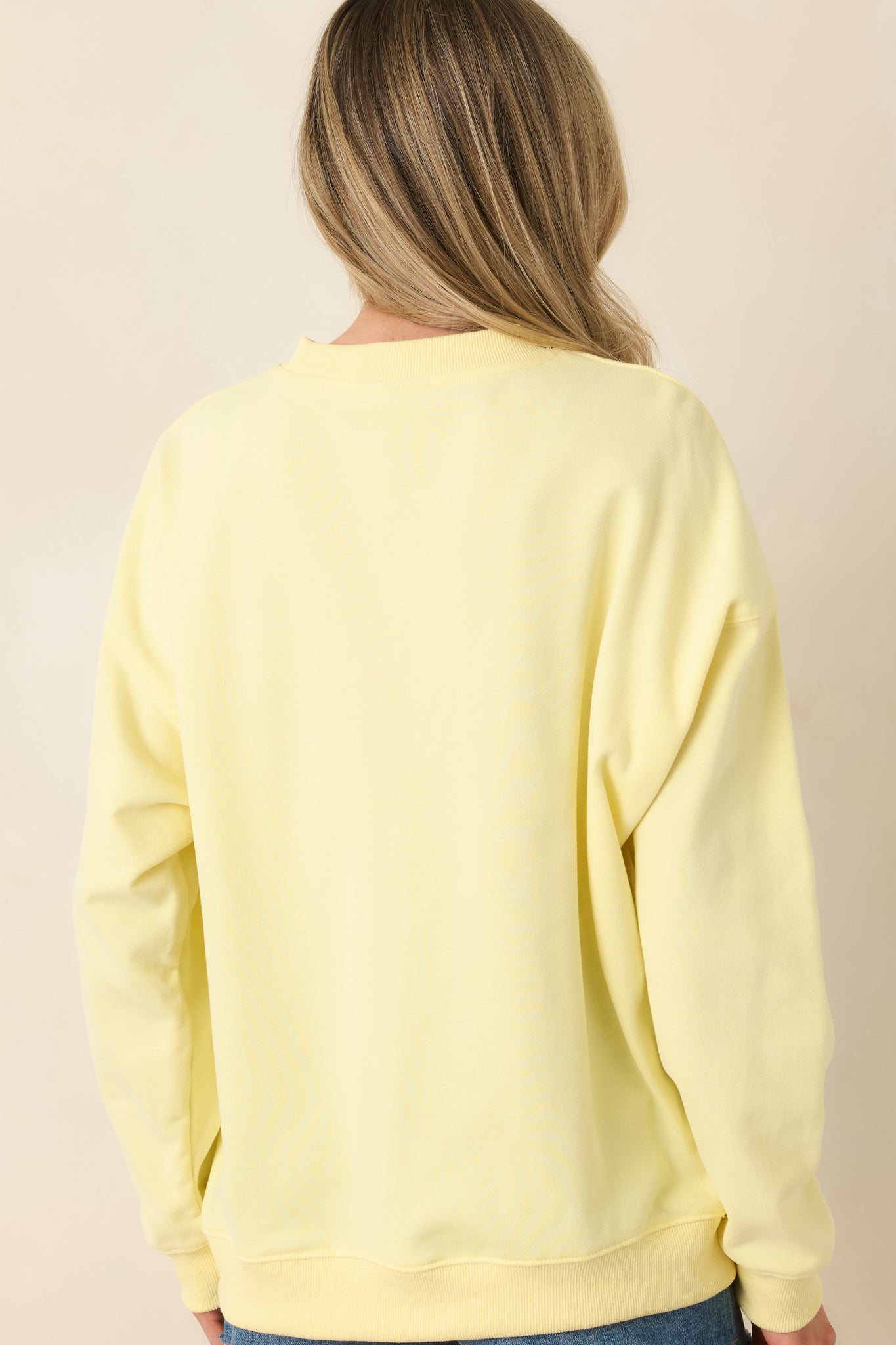 Back view of yellow crewneck sweatshirt displaying long sleeves, relaxed fit, and ribbed hem.