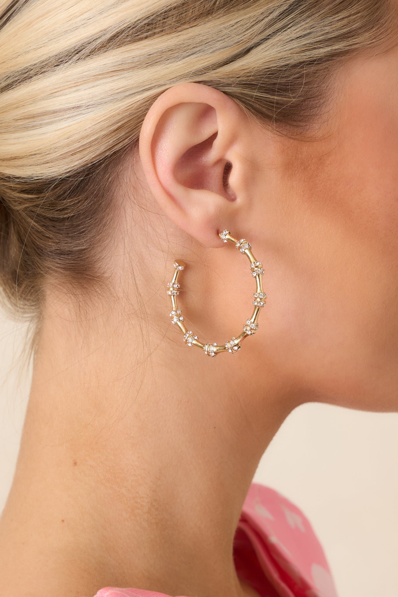 Close-up of gold hoop earring detailing small faux diamond accents and post back closure hardware.