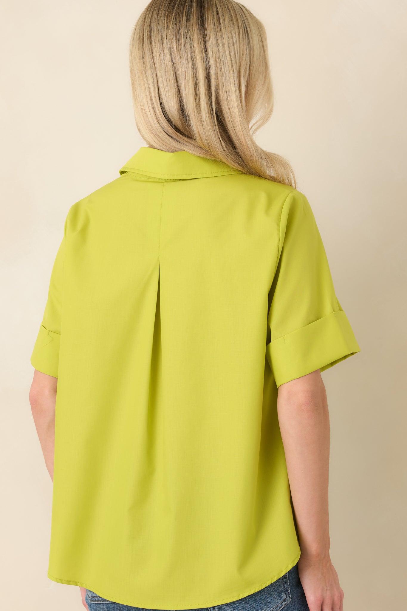 Rear view of the chartreuse green blouse displaying a subtle back pleat, cuffed short sleeves, and gently rounded hem for added movement.