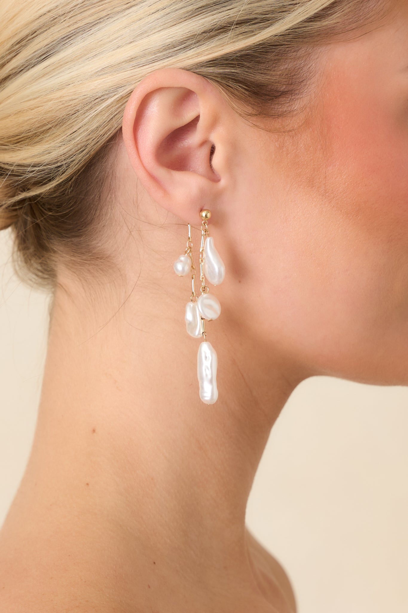 Detail of gold and pearl drop earrings highlighting layered chain strands and textured pearl shapes.