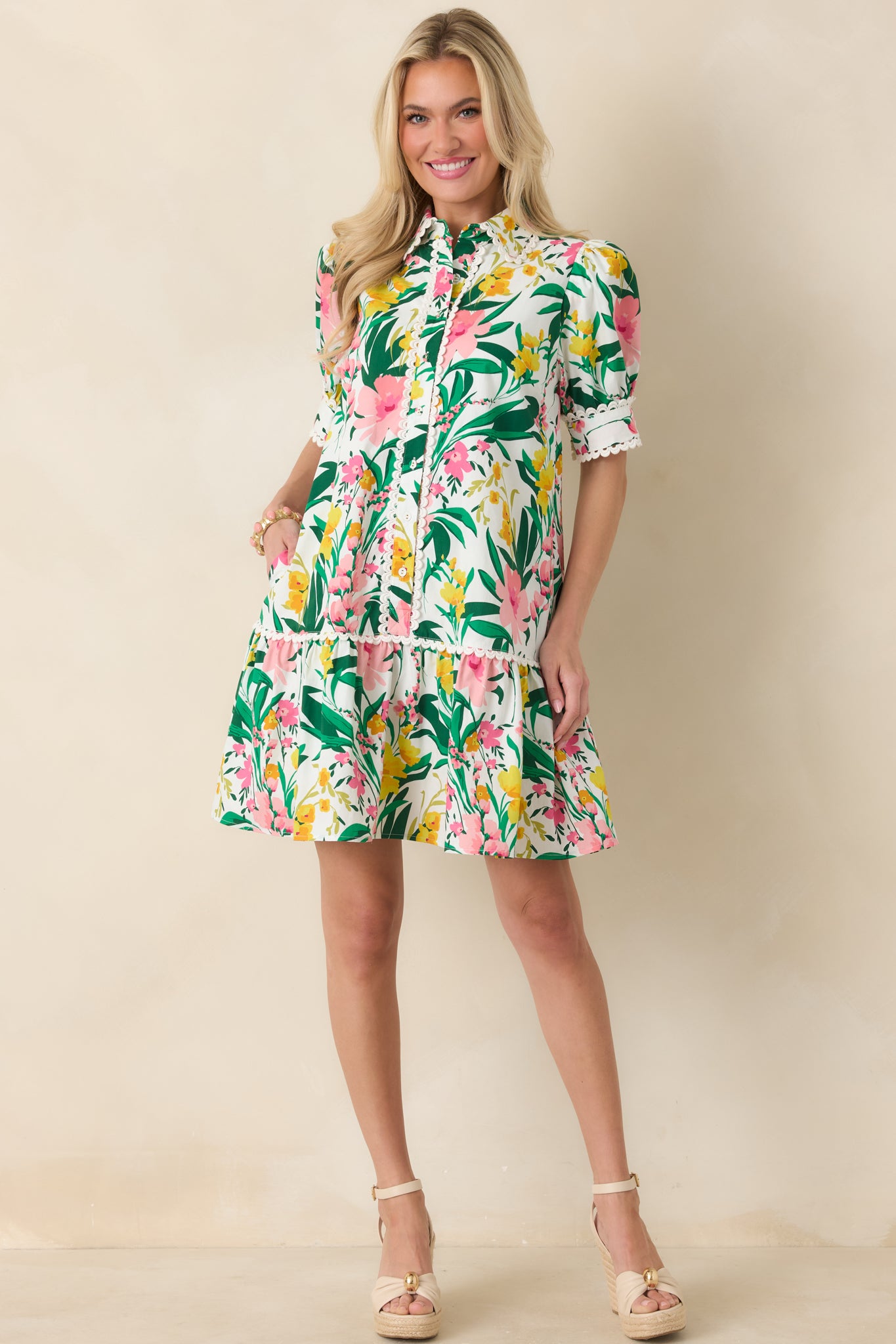 Mini dress with vibrant green, pink, and yellow floral print, tailored button-front bodice, scalloped trim along neckline and placket, puff sleeves, and flouncy ruffle hem.