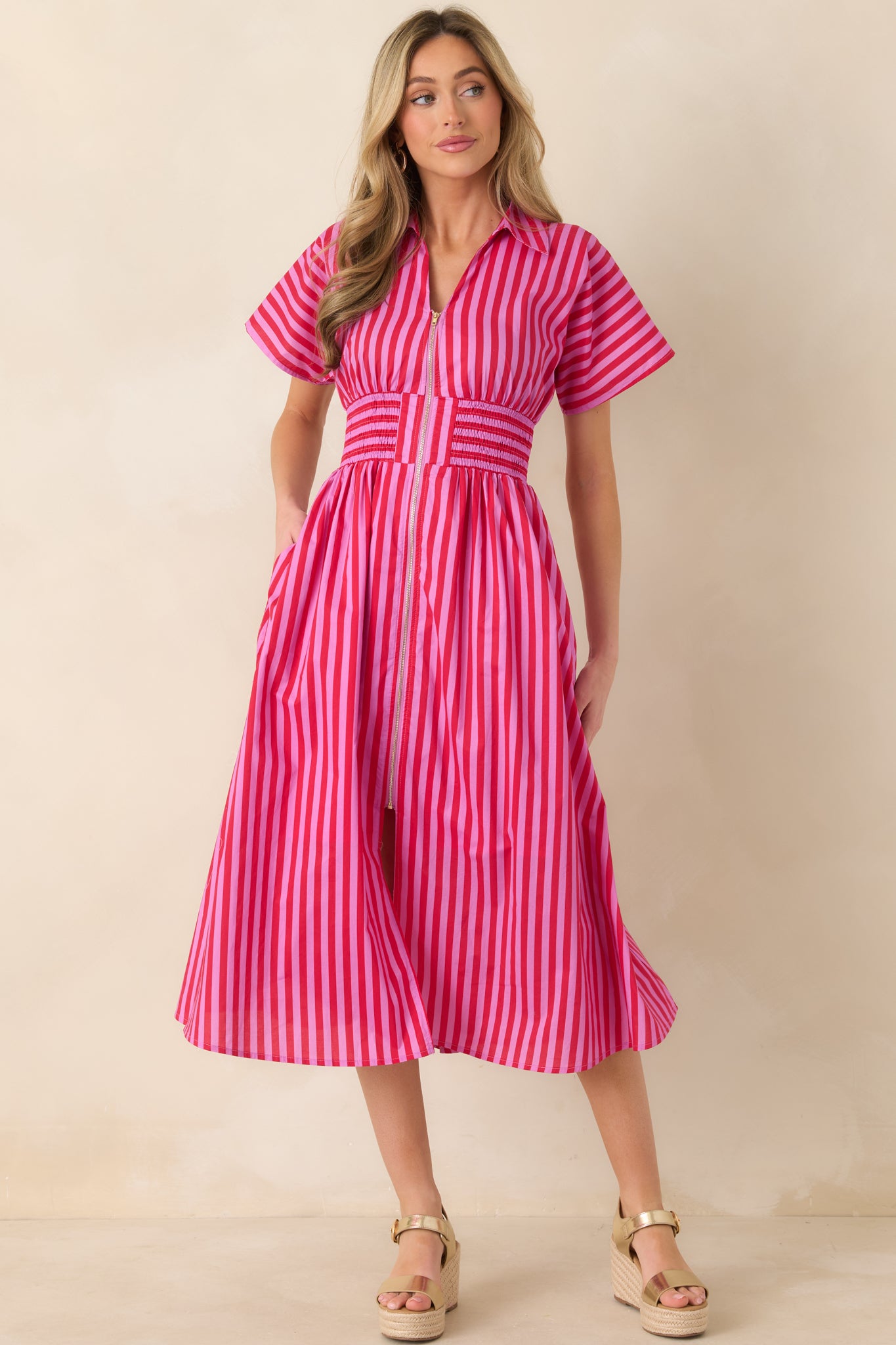 Pink and red striped midi dress with zip-front closure, collared neckline, short sleeves, and a wide smocked waistband flowing into a full A-line skirt.