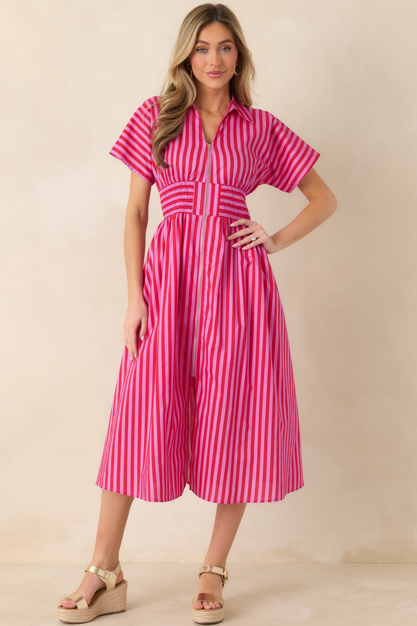Cotton midi dress in pink and red stripes showcasing a collared neckline, front zipper closure, defined smocked waist, and full skirt with volume.
