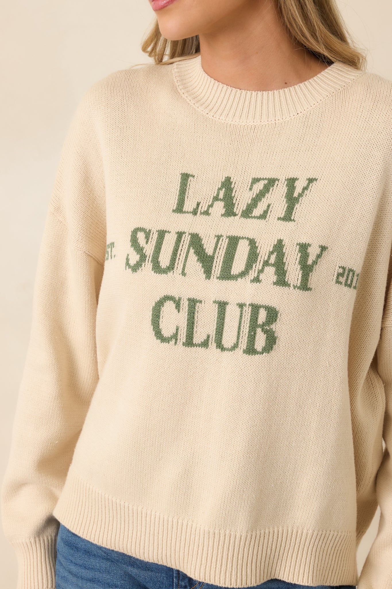 Close look at the ribbed hems, knit fabric, and bold green lettering on the ivory pullover.