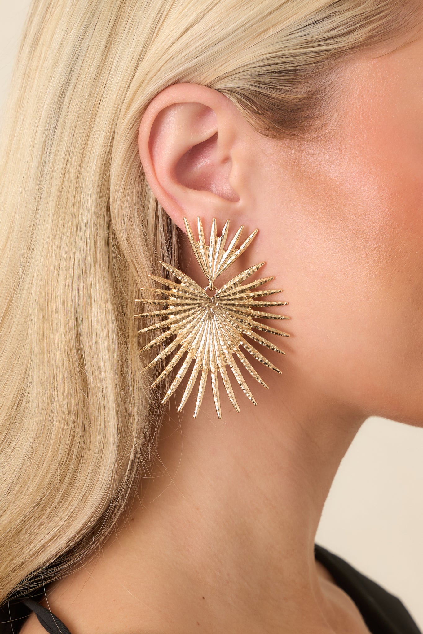 Close-up of the sculptural fan earrings showing intricate texture, layered design, and polished gold finish.