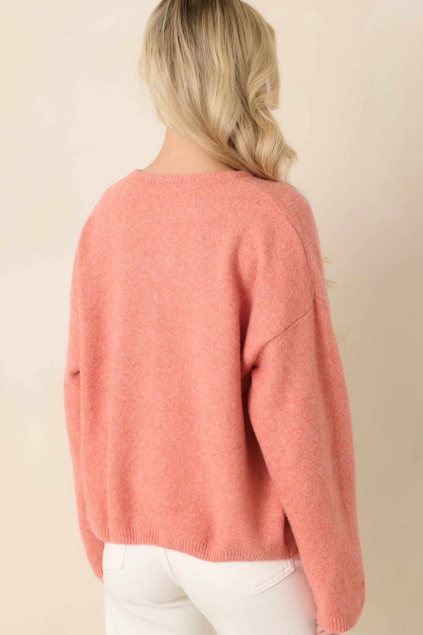 Rear view of the orange cardigan highlighting the relaxed silhouette, smooth knit texture, and clean ribbed detailing along the hem and sleeves.