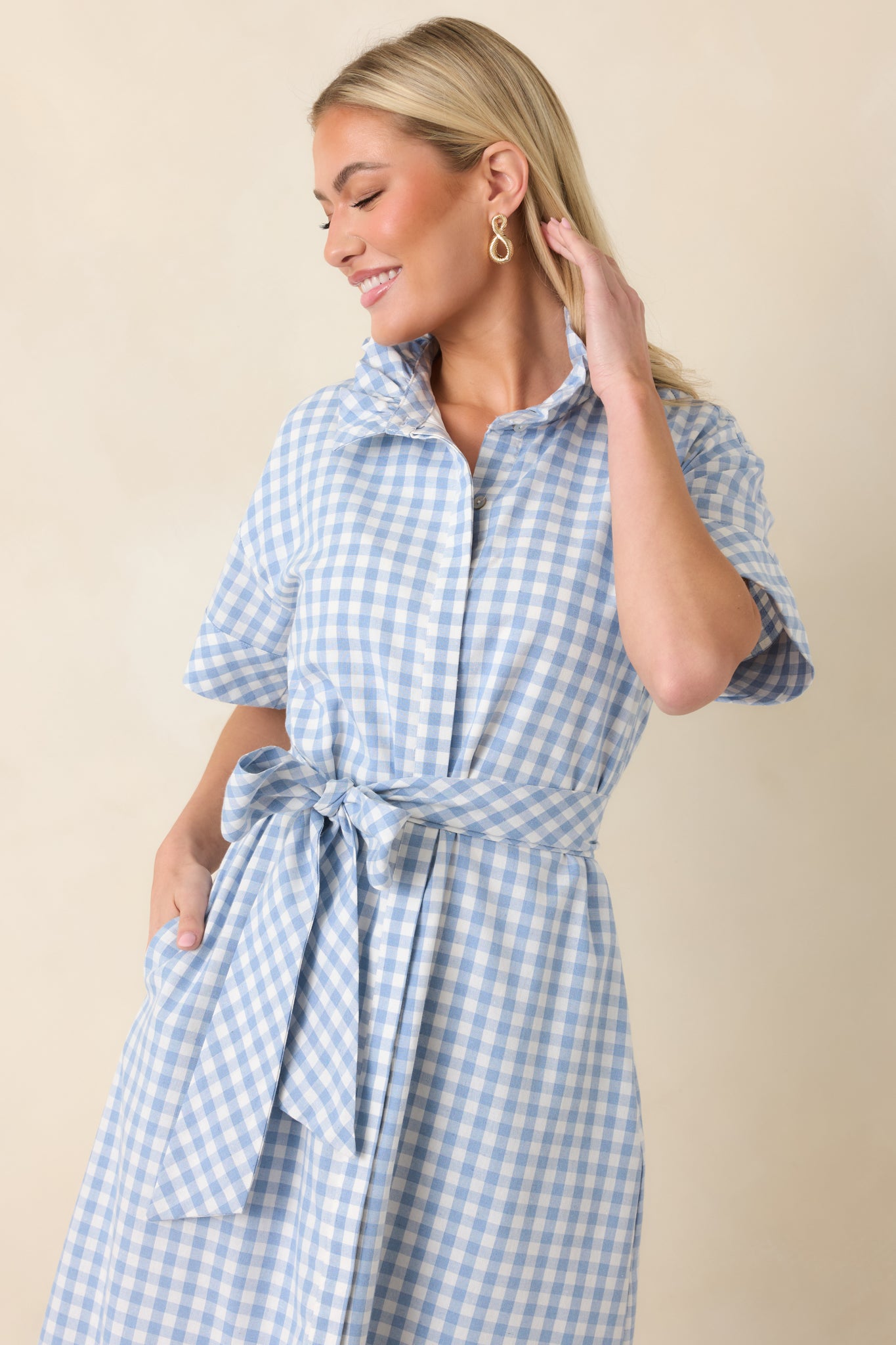 Close-up of the blue and white gingham fabric showing button placket, ruffle collar, and fine stitching detail.