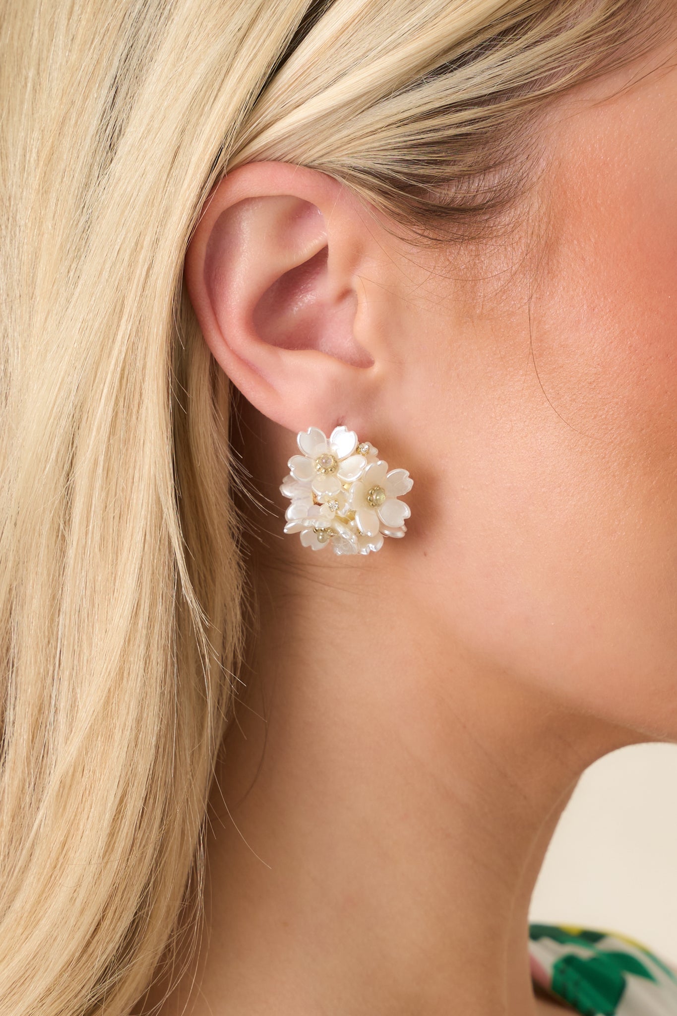 Close-up of a gold hoop earring with pearlescent petals and sparkling crystal centers, highlighting delicate floral detailing.