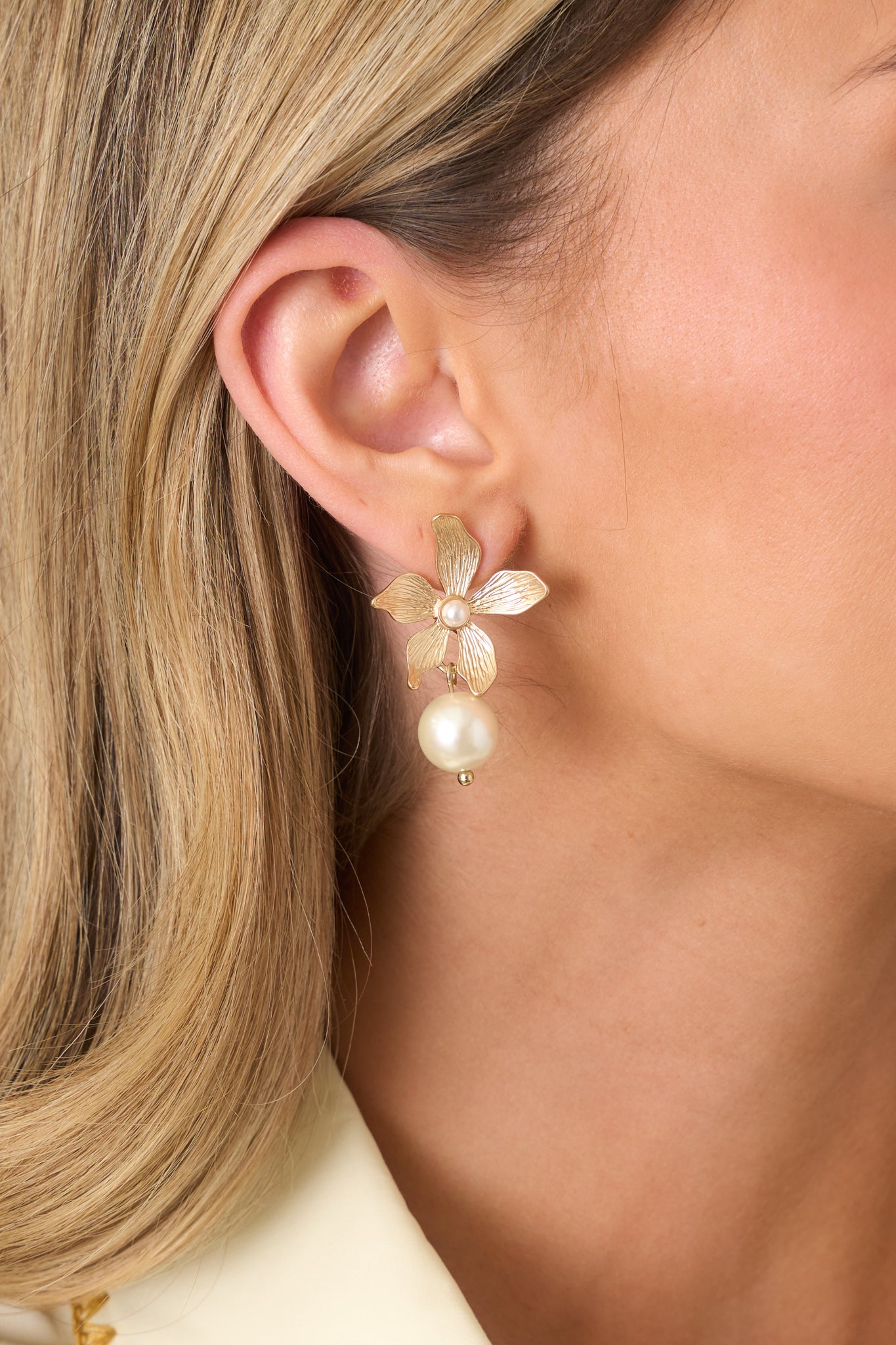 Close-up shot of earrings highlighting sculpted gold flower and graceful dangling pearl.