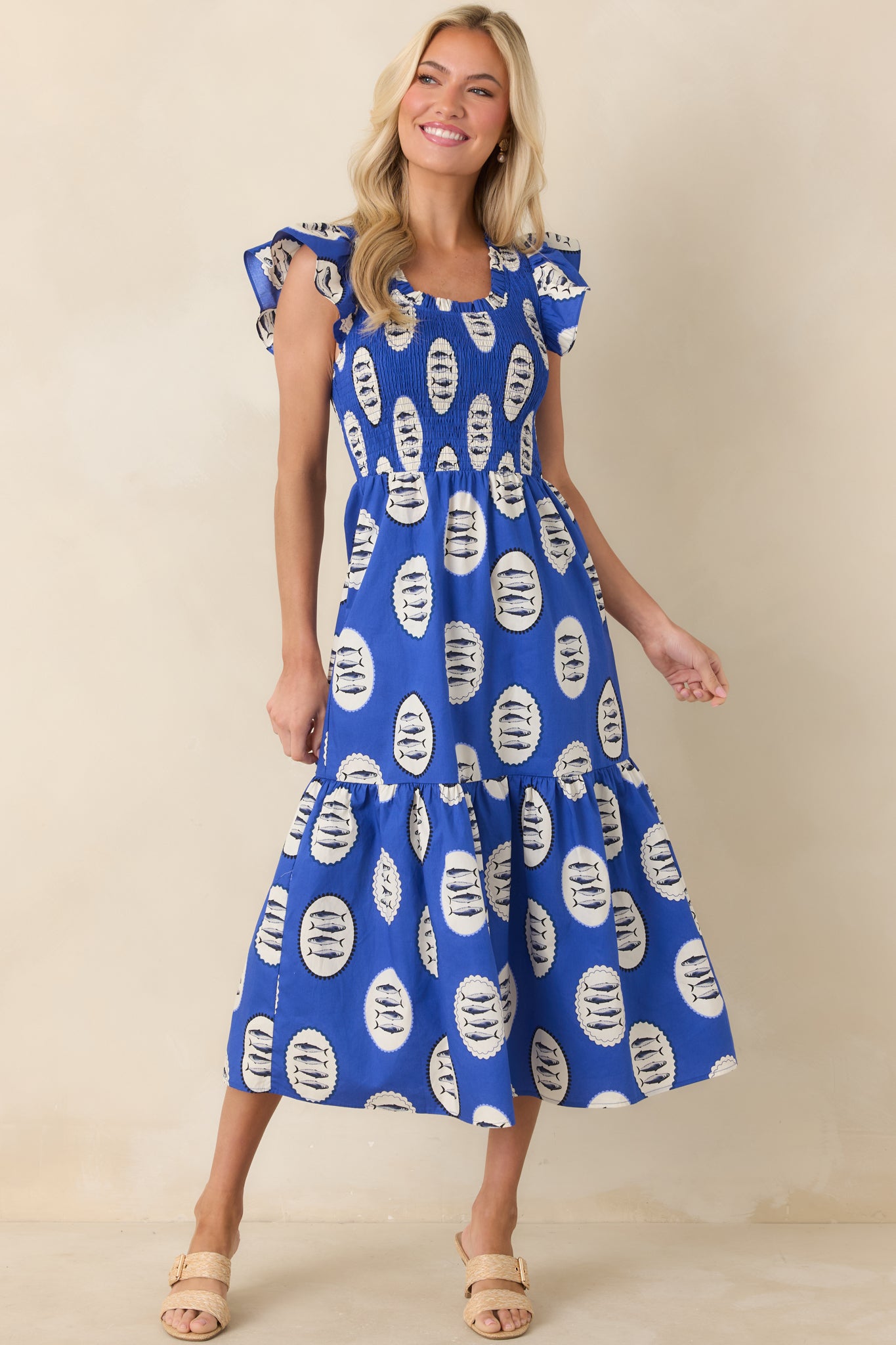 Bright royal blue fish print dress crafted from lightweight cotton, showcasing textured smocking through the bodice and a softly gathered tiered skirt.