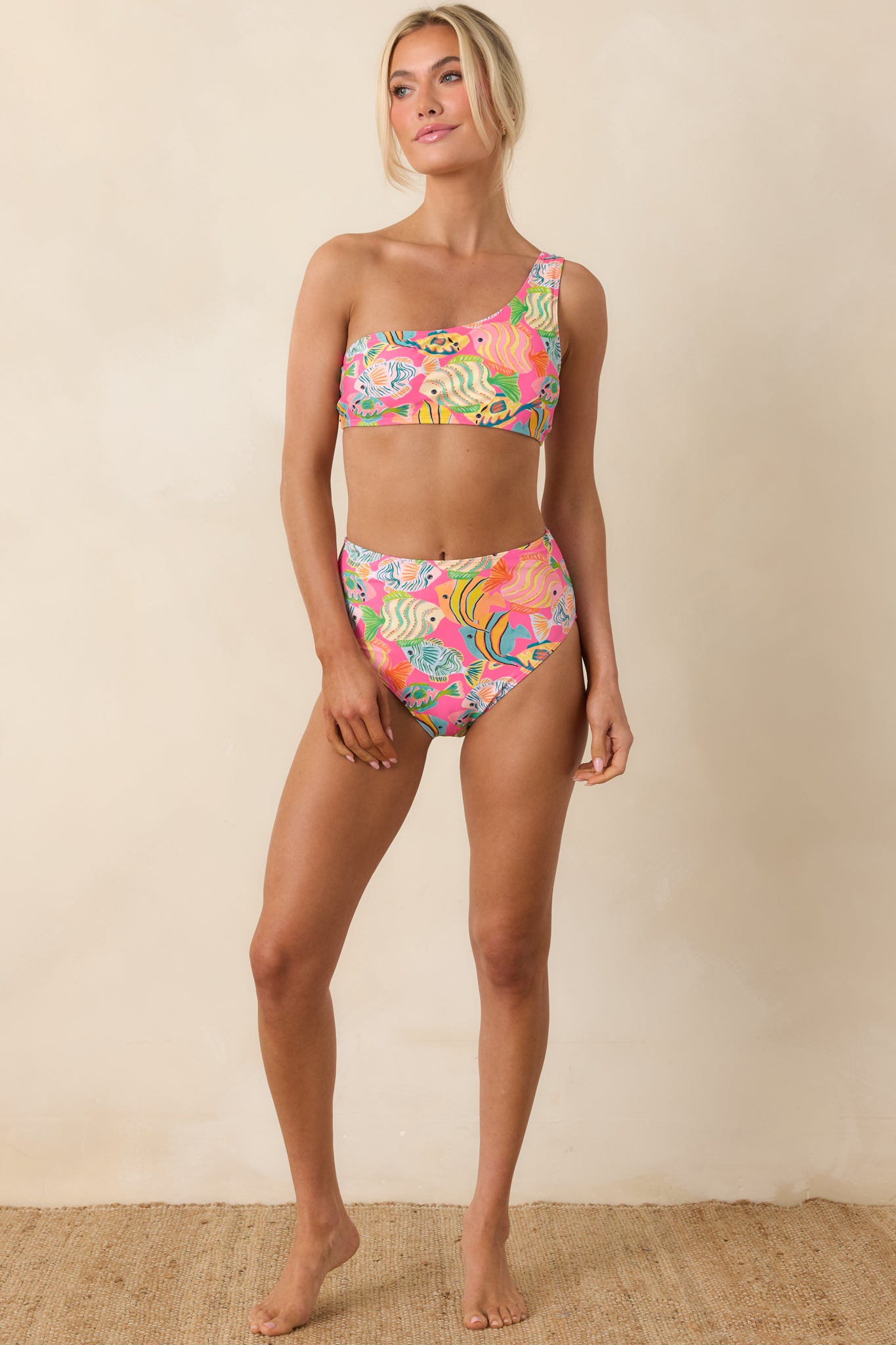 Full-length front view of high-waisted bikini bottoms in bright pink with playful tropical fish print.