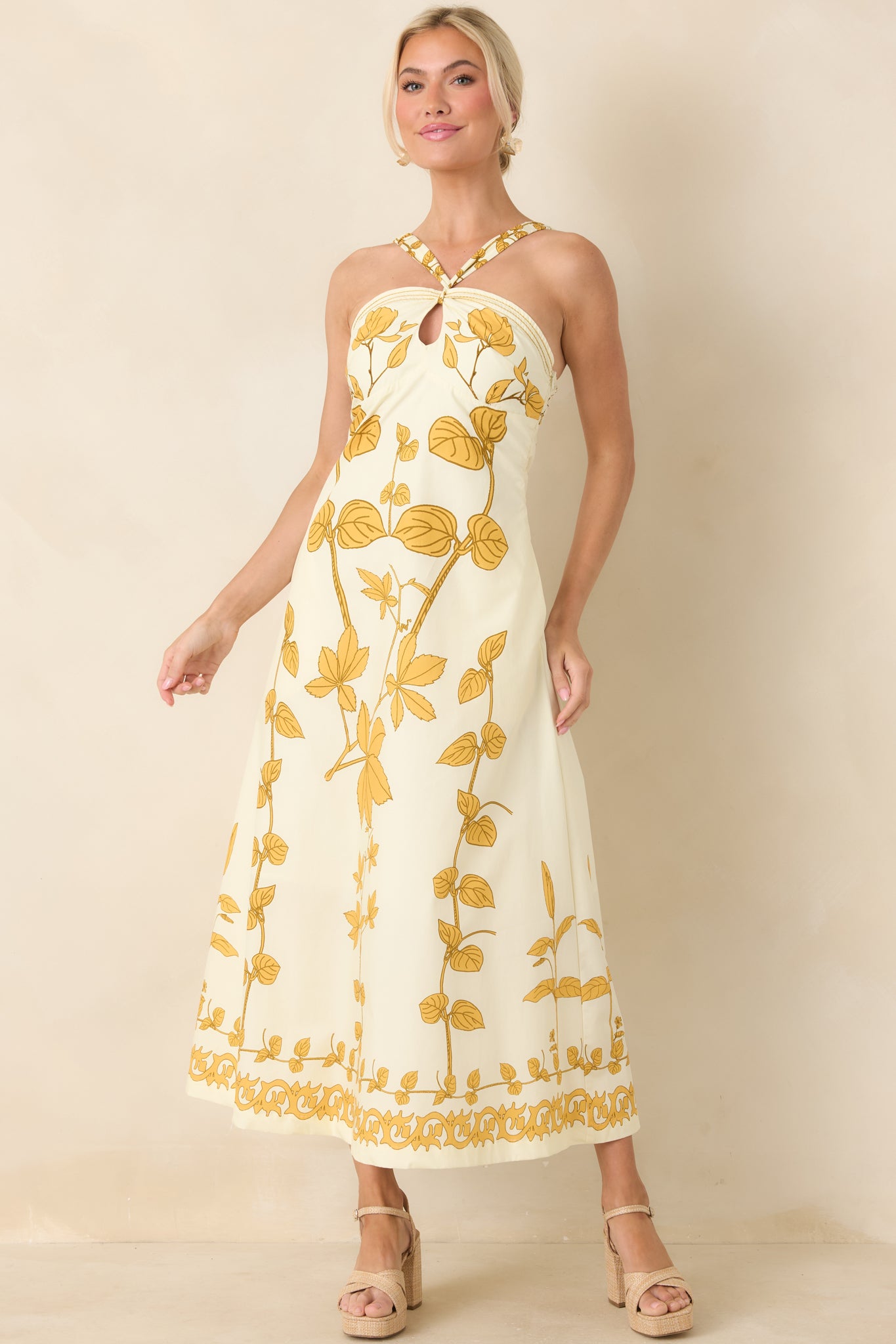 Front view of an ivory maxi dress with honey gold floral print, halter neckline, keyhole detail, and flowing full-length skirt.