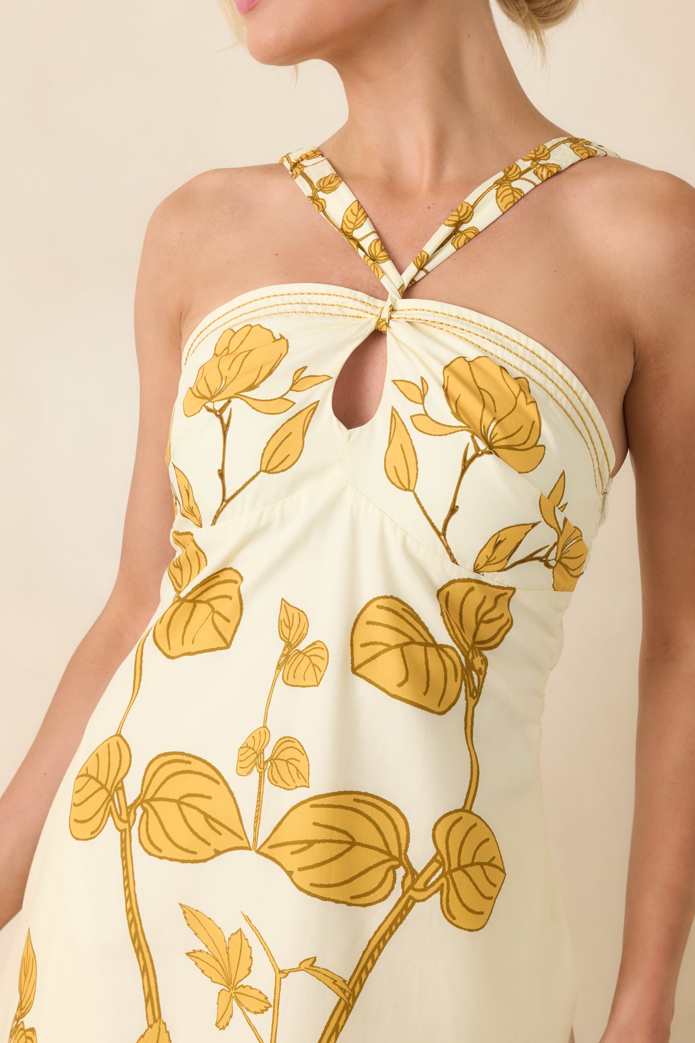 Close-up of ivory cotton fabric with honey gold floral print, halter neckline, keyhole detail, and textured border trim.