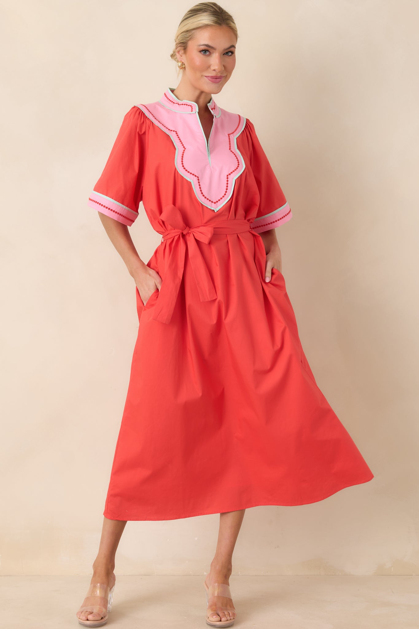 Bold red and pink trimmed midi dress featuring a scalloped V-neck, short flutter sleeves, and a removable tie belt that enhances the structured yet playful shape.