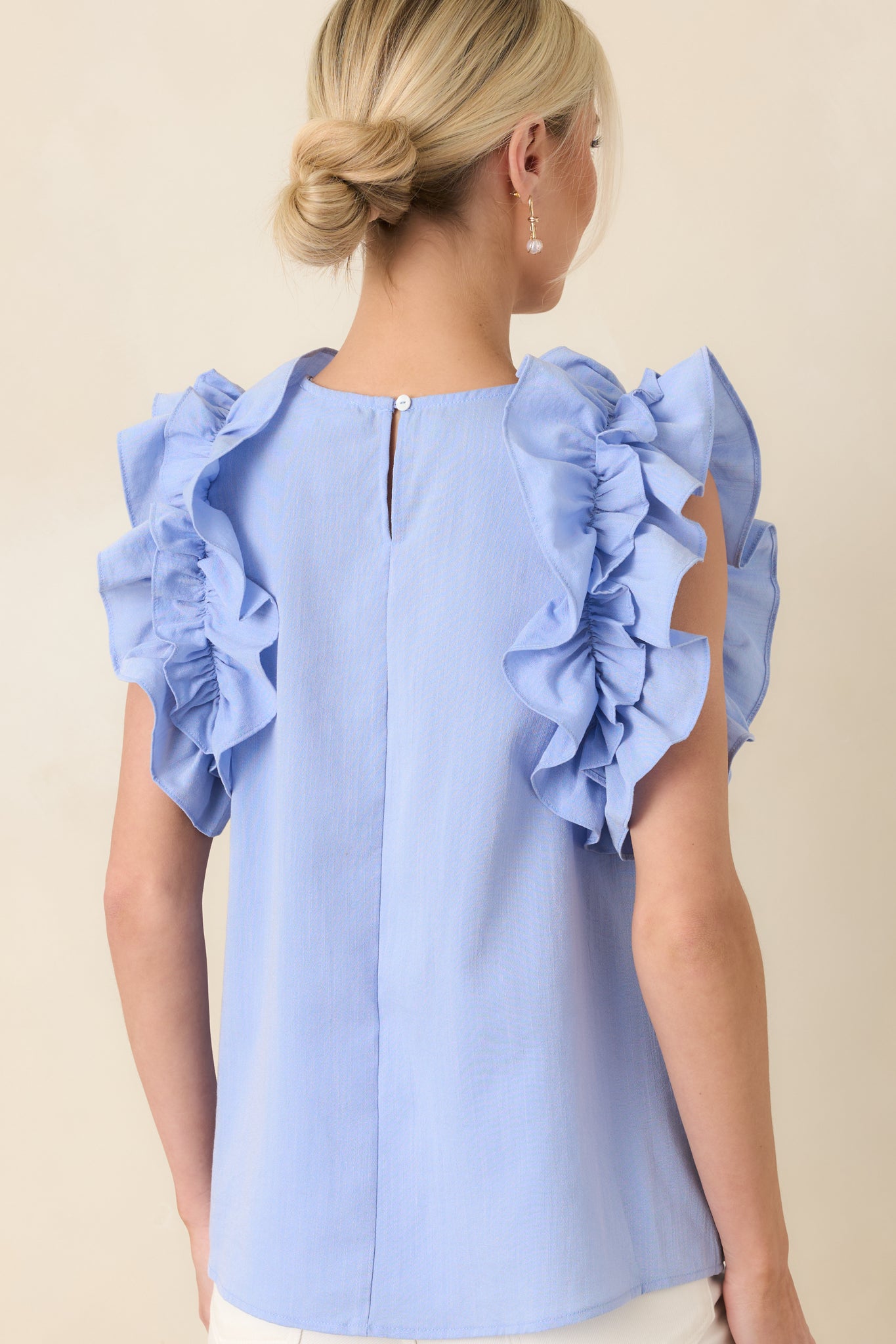 Rear view of light blue top with keyhole opening and button closure at neckline.