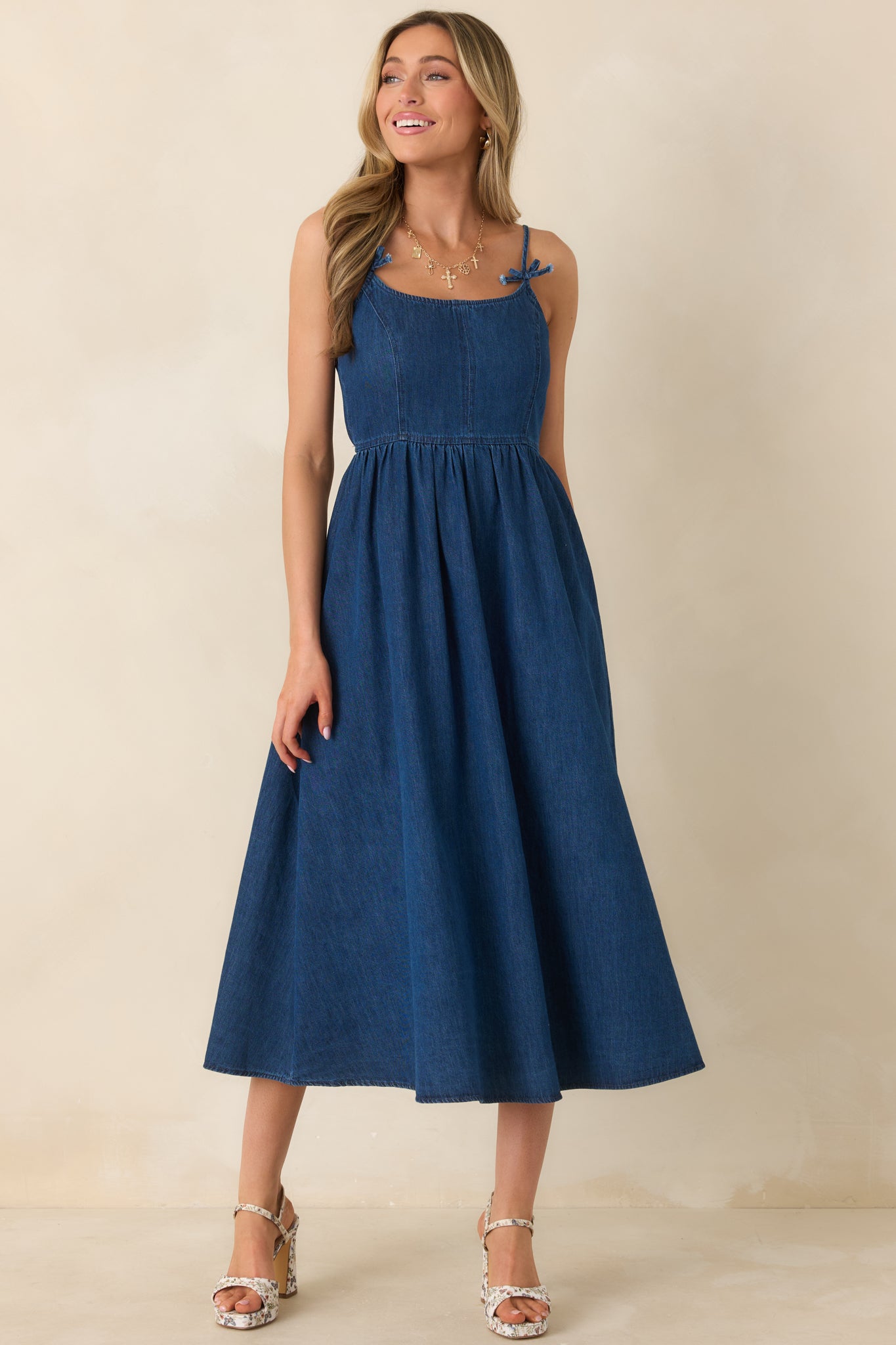 Dark wash midi dress with adjustable spaghetti straps tied in delicate bows, featuring a fitted bodice and a flowing gathered skirt.