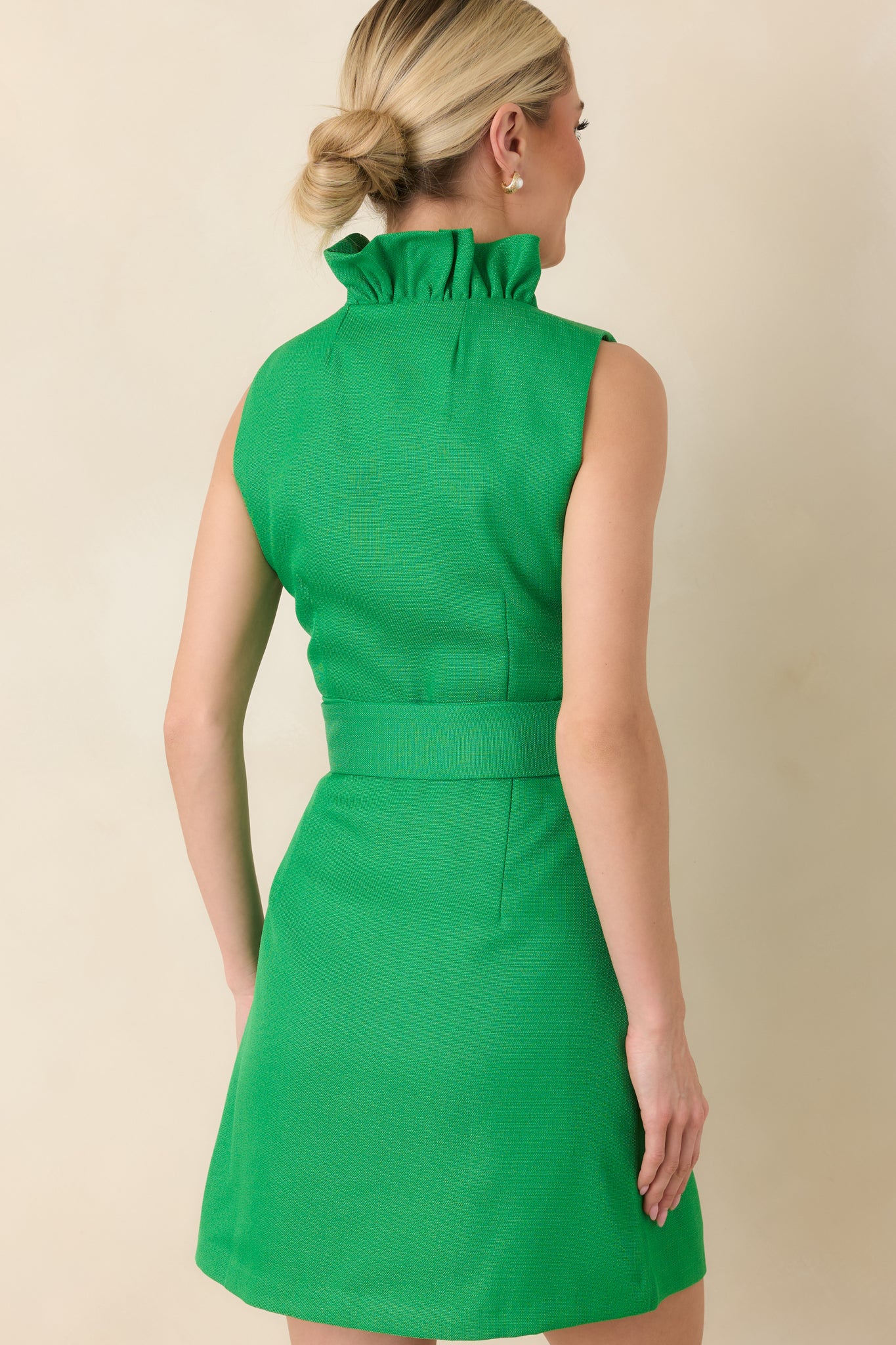Rear view of the green mini dress showing the fitted waist, coordinating belt, and smooth, sleek silhouette.