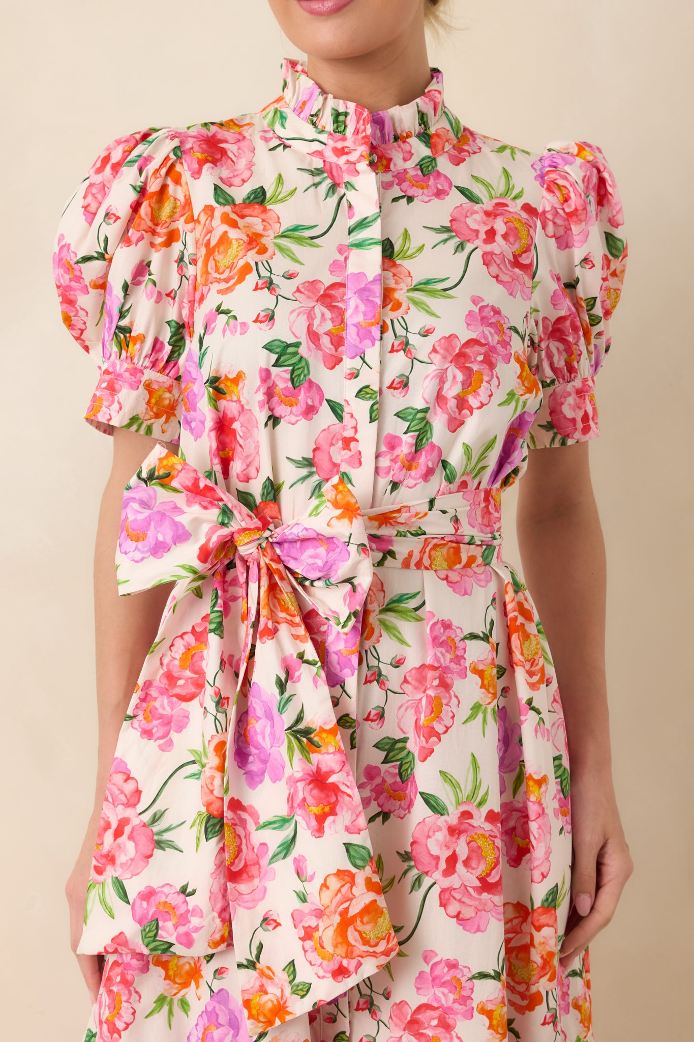 Detailed view of the pink floral fabric highlighting the ruffled high neckline, puffed sleeves, and adjustable waist tie.