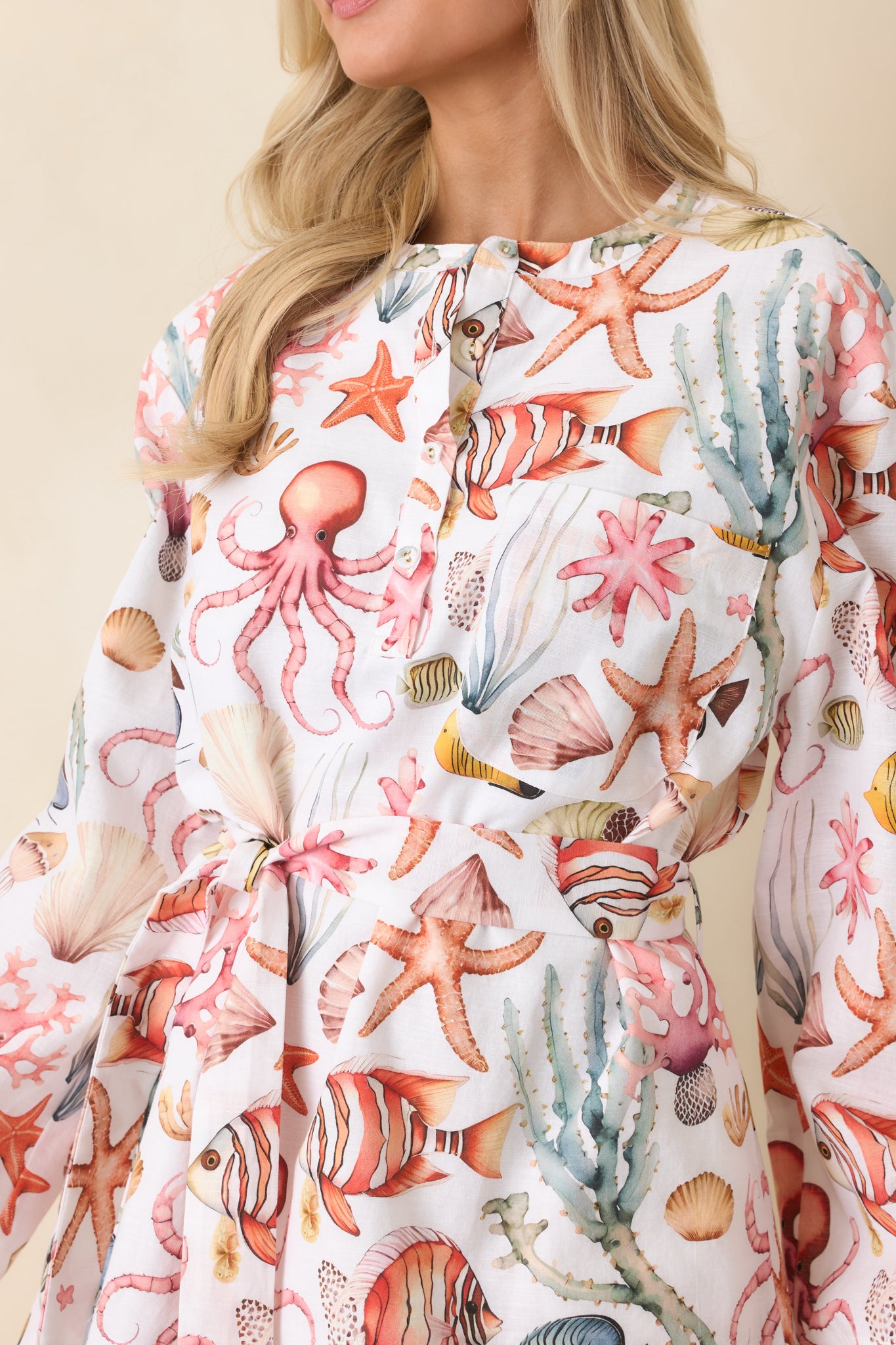 Cotton-linen texture showing partial button-front closure, roll-tab sleeve, and multicolor coastal print.