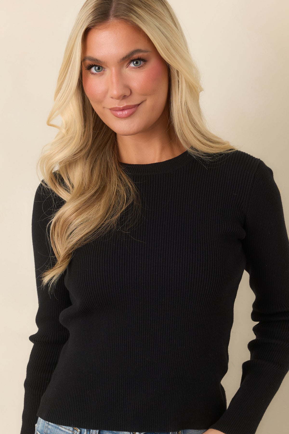 The fitted black top finishes with a simple straight hem that works well tucked into trousers, denim, or skirts.