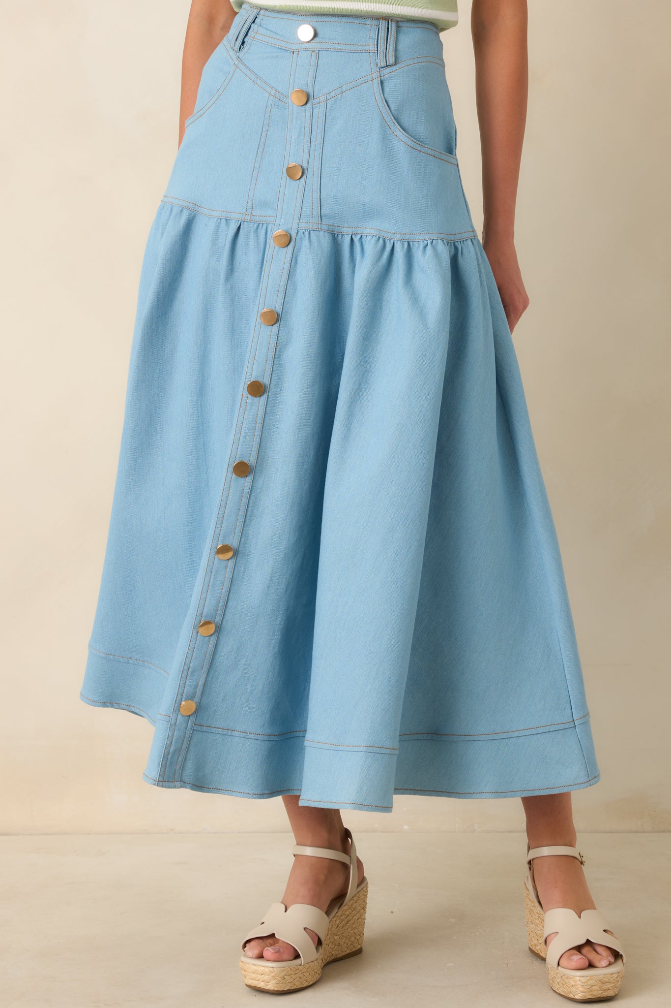 Light wash denim skirt highlighting high-rise waistband with belt loops and gold-tone button front closure.