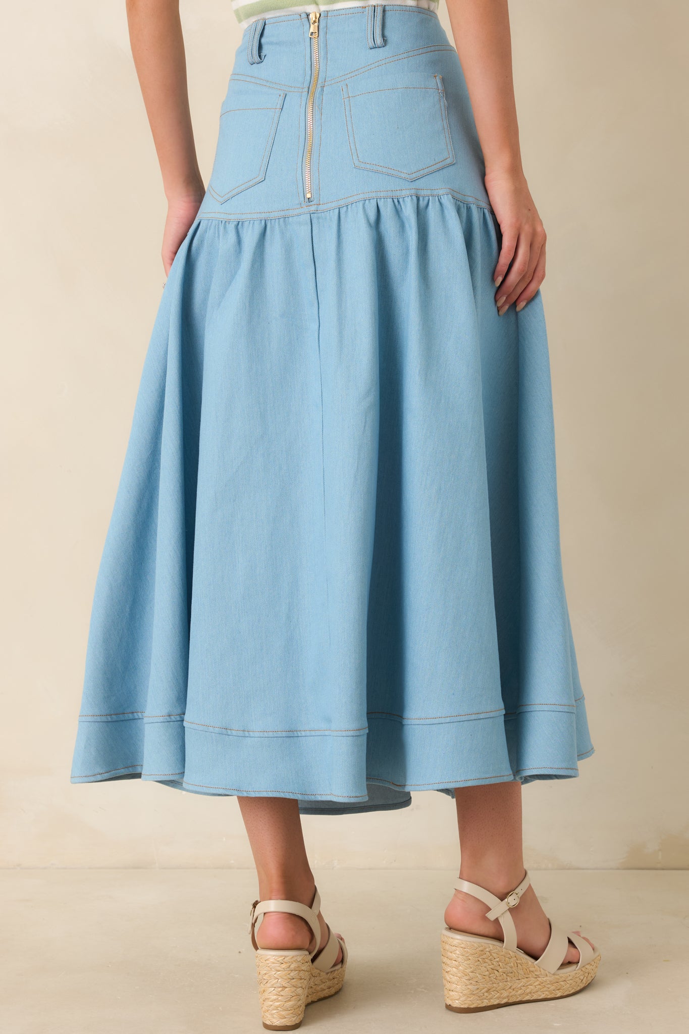 Rear view of light wash denim maxi skirt featuring back pockets, structured waistband, and zipper closure detail.