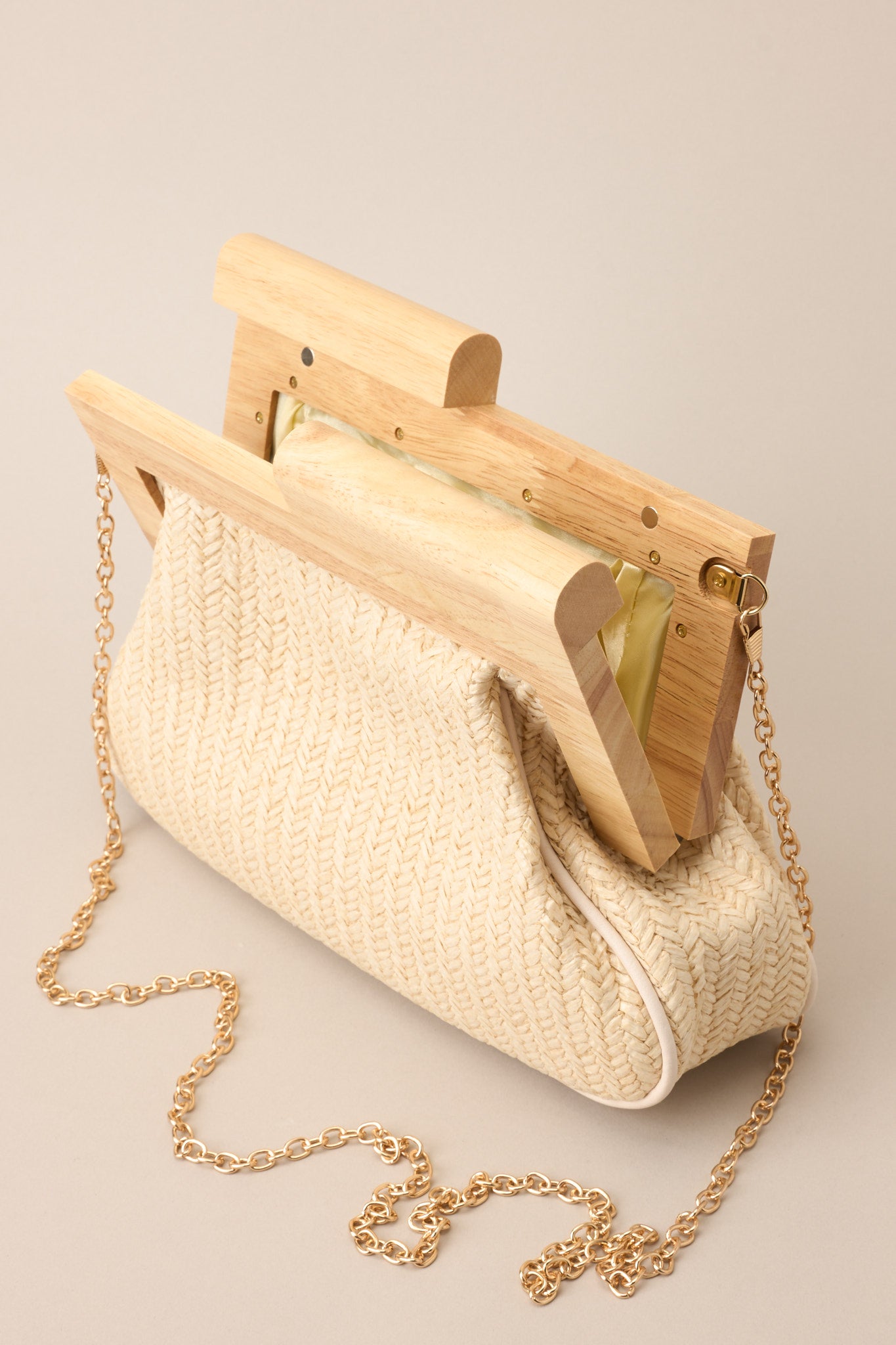 Open view of this ivory rattan clutch with a wooden handle and metallic closure.