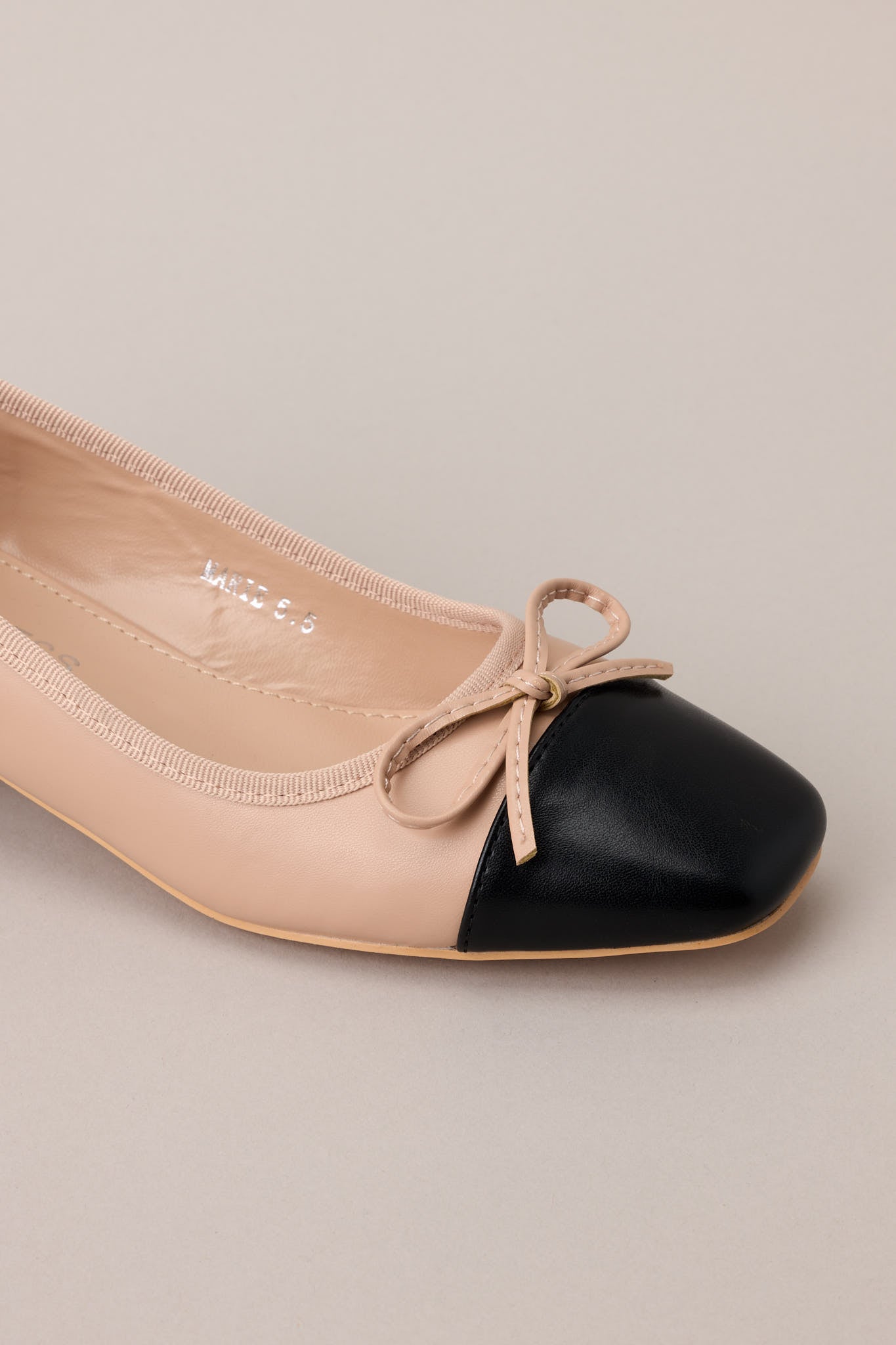 Super close-up of the bow detail and color block stitching across the front strap of the beige heel.