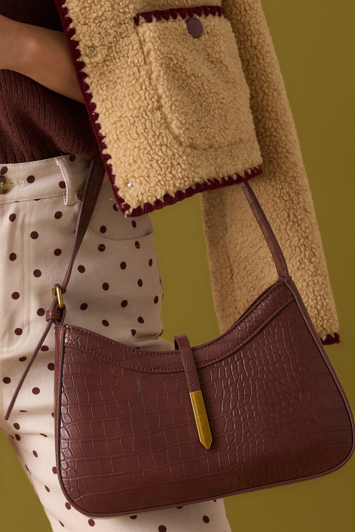Brown, croc handbag in front of an olive backdrop.