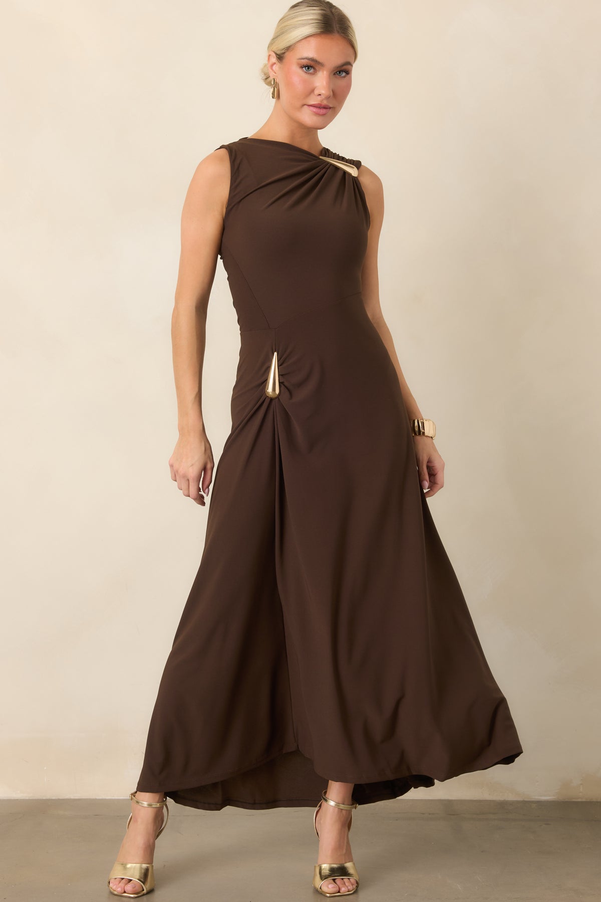 Woman in a brown, sleeveless dress, with gold details at the hip and shoulder.