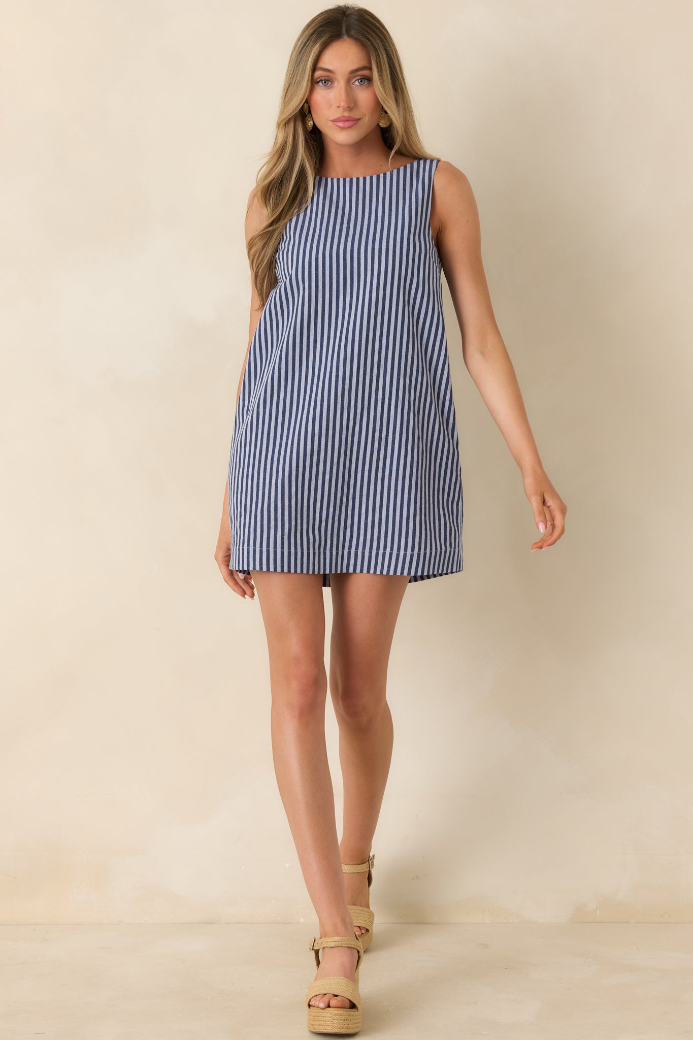 Sleeveless mini dress featuring structured drape and high neckline in timeless pinstripe.