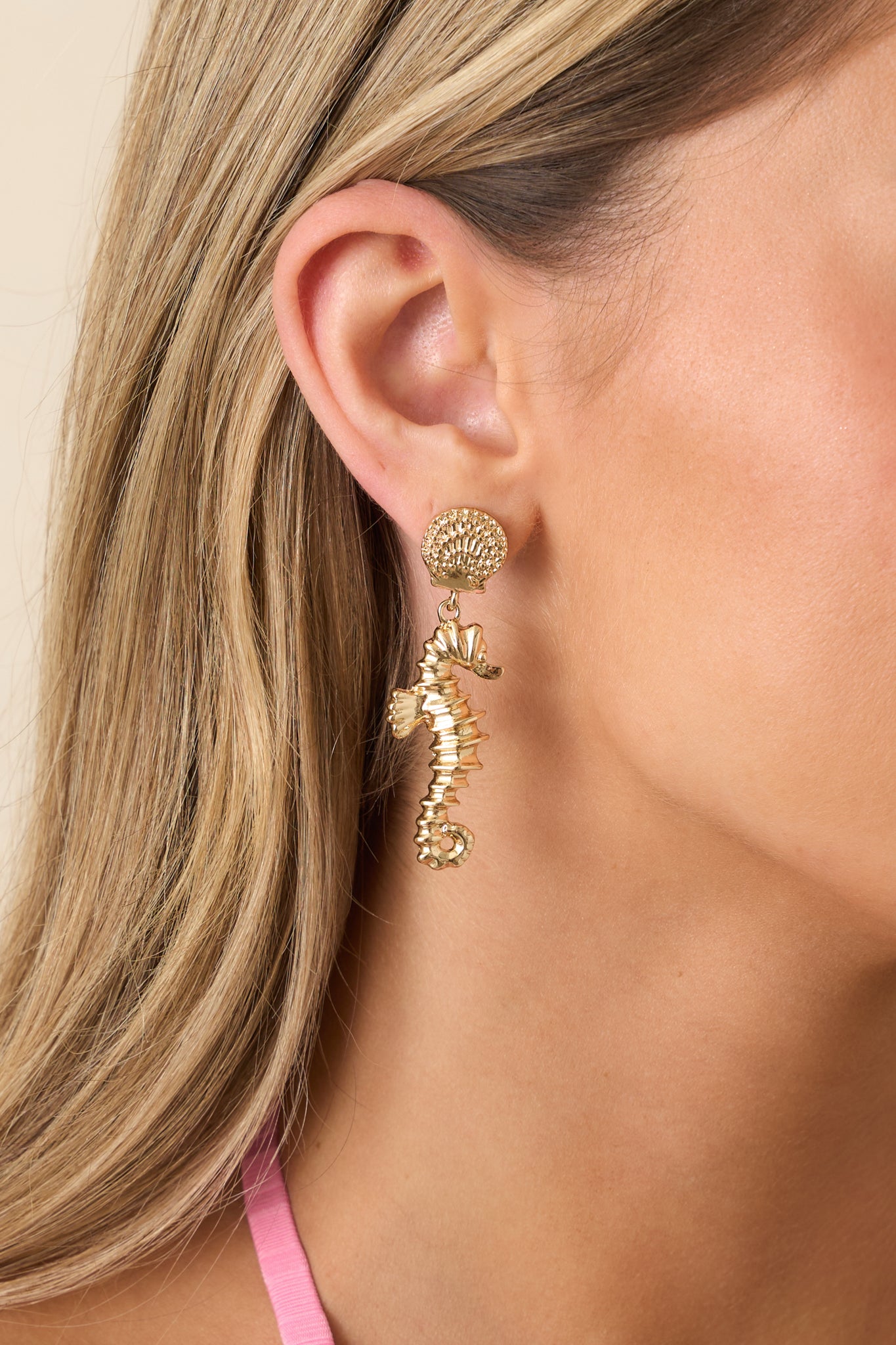 Detailed close-up of gold earrings showcasing the shell-inspired stud texture and intricately designed seahorse drop.