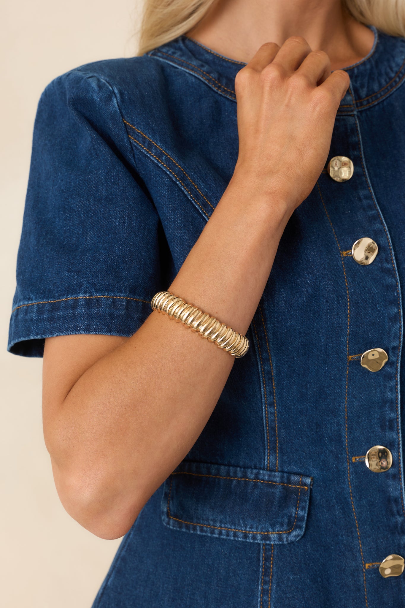 Close-up detail of gold bracelet showing ribbed texture, stretch band, and polished finish.