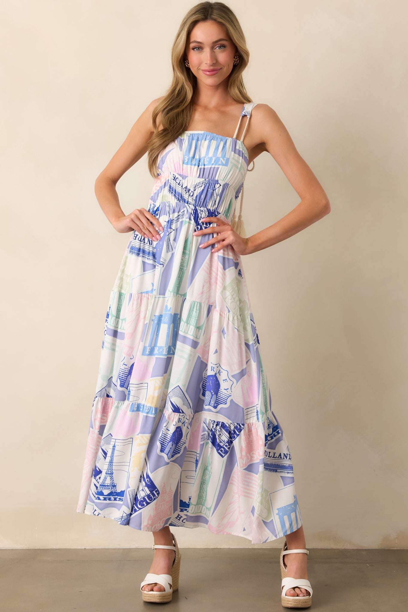 A blue midi dress with a multicolor passport-inspired print, featuring an elastic square neckline and a tiered skirt for a flowing silhouette.