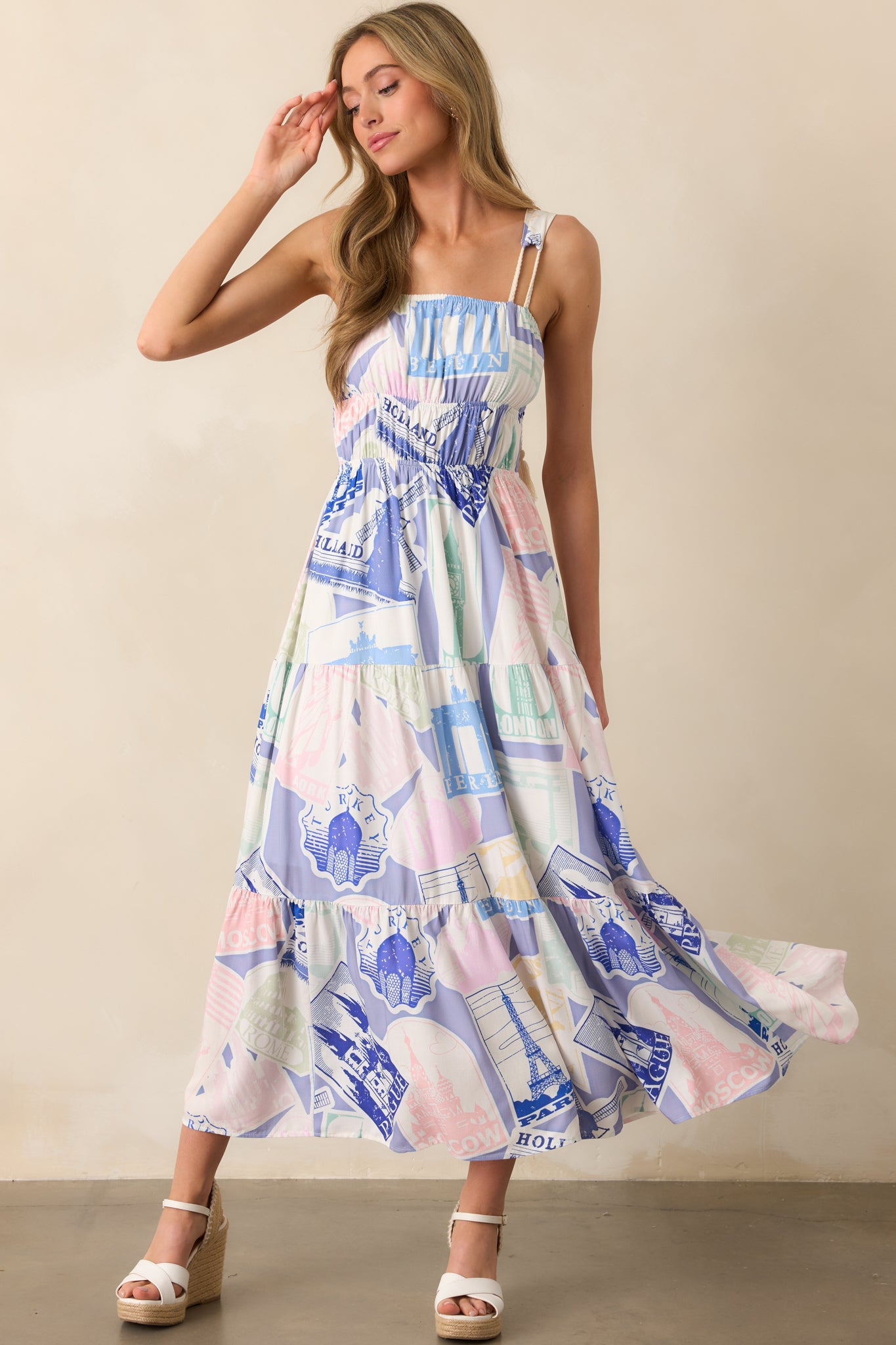 A lightweight blue midi dress with a tiered skirt, elastic neckline, and intricate tassel tie straps adding texture and movement.